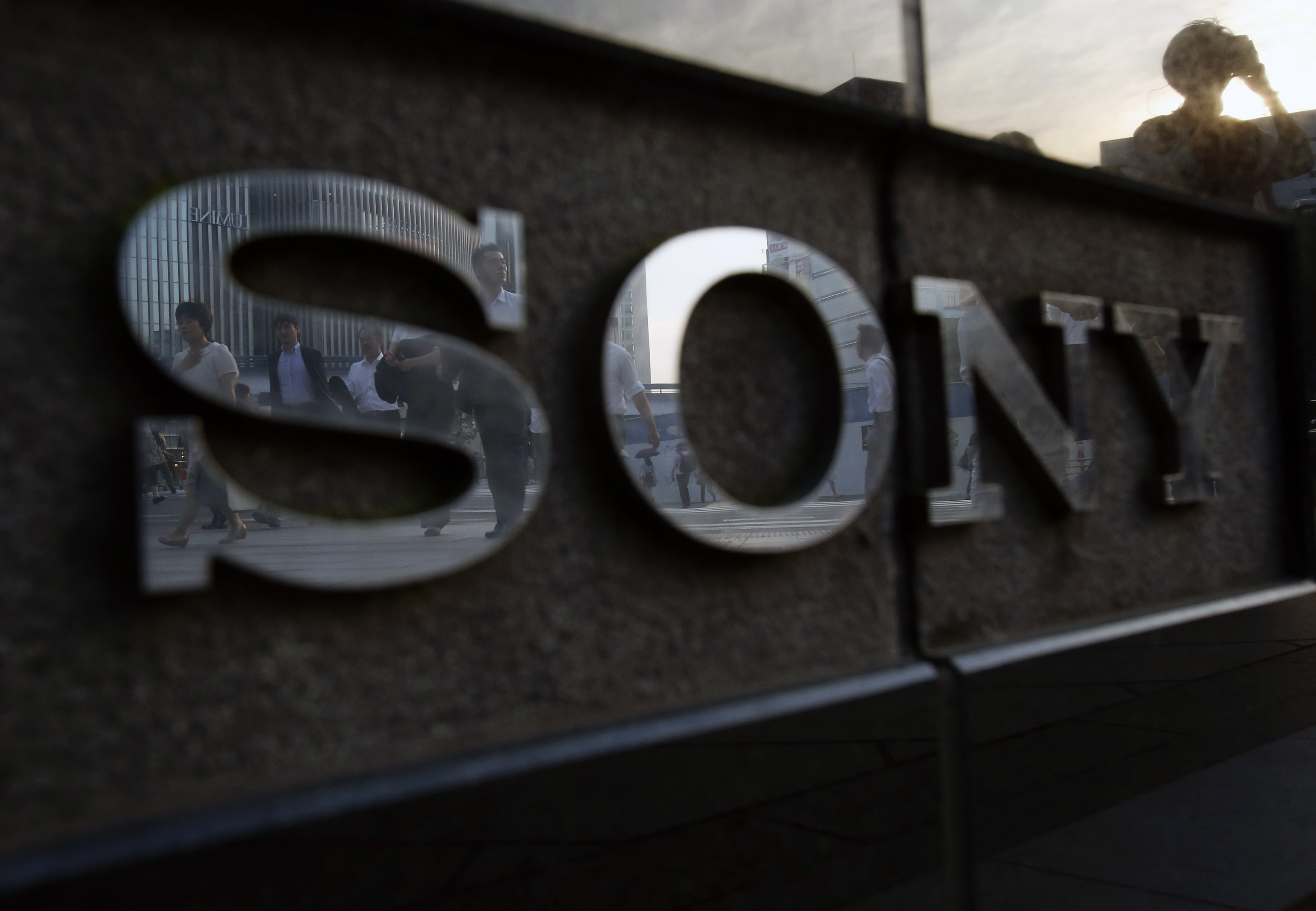Pedestrians are reflected in a logo of Sony Corp outside its showroom in Tokyo