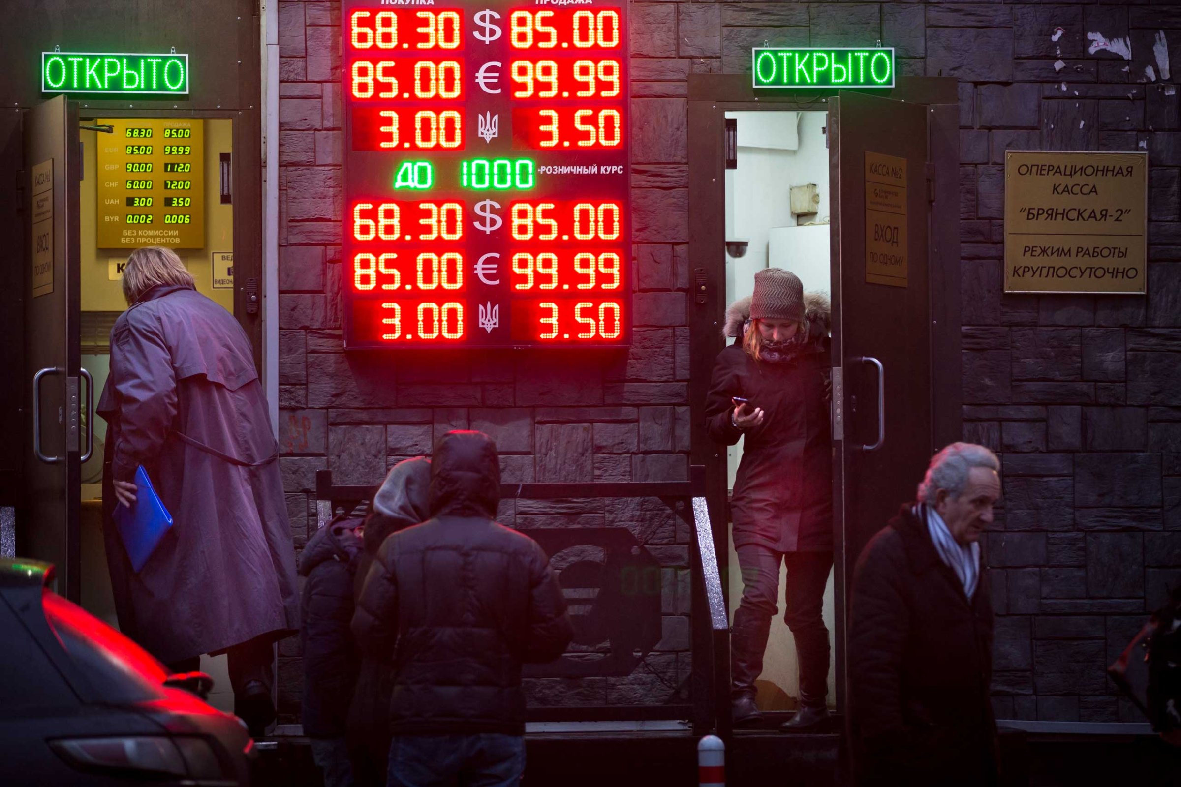 People wait to exchange their currency as signs advertise the exchange rates at a currency exchange office in Moscow, Dec. 16, 2014.
