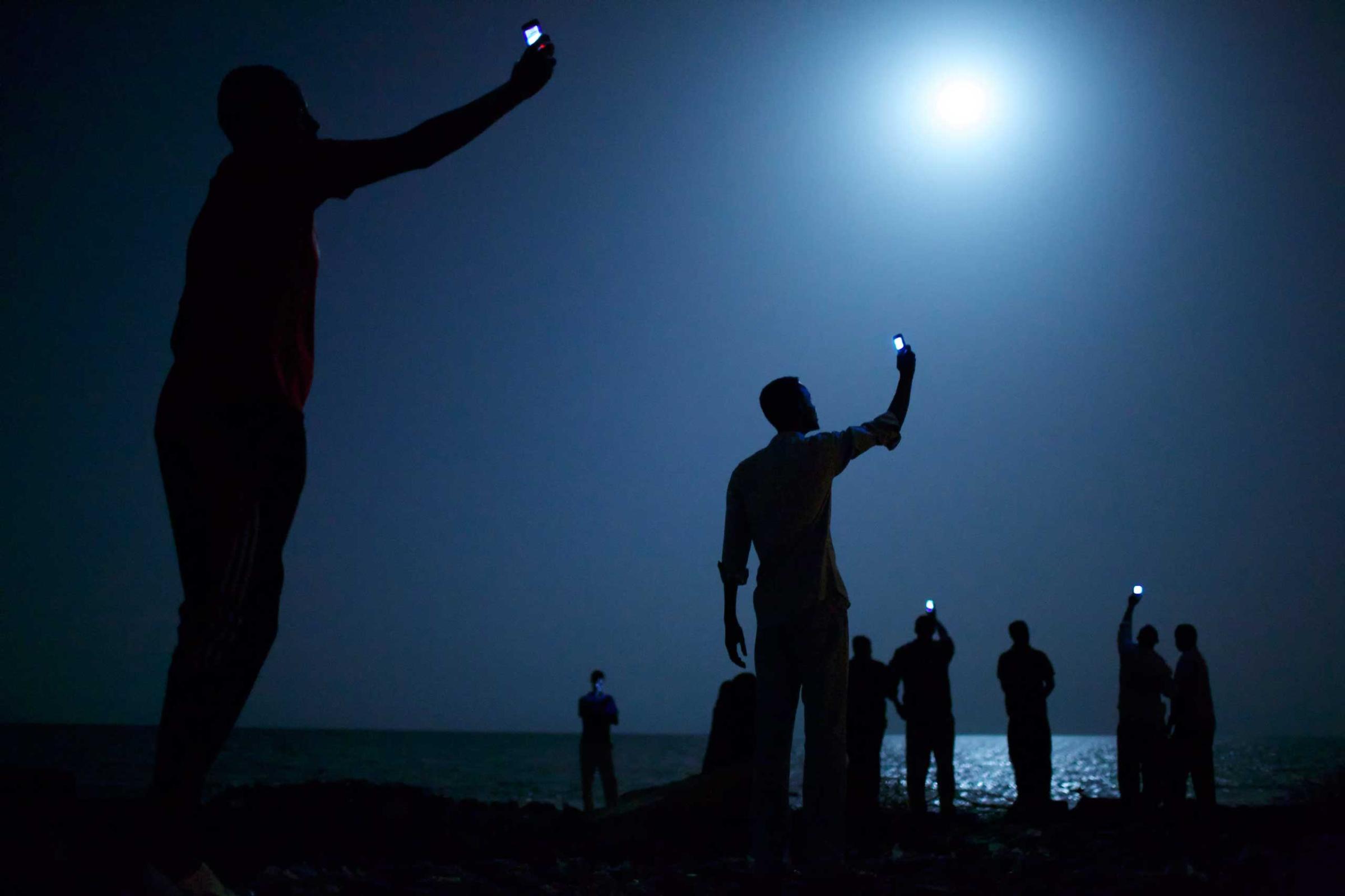Somali's wave their mobile phones doing what is known among locals as 'Catching,' in an attempt to catch or pickup the mobile phone tower in neighboring Somalia as they stand on Khorley Beach, also called Dead Water Beach, in Djibouti City, Djibouti, Feb. 26, 2013. As a means to stay in contact with their family and friends back home, one purchases a Somalia SIMM card from the black-market in Djibouti City, placing the SIMM in mobile phone and swinging about the phone in specific areas where a signal might be caught. The best time to catch the signals are at night. Djibouti City to the border of Somalia where the nearest Somali cell tower is located is only roughly 30 miles (48 kilometers) south of the capital of Djibouti.555