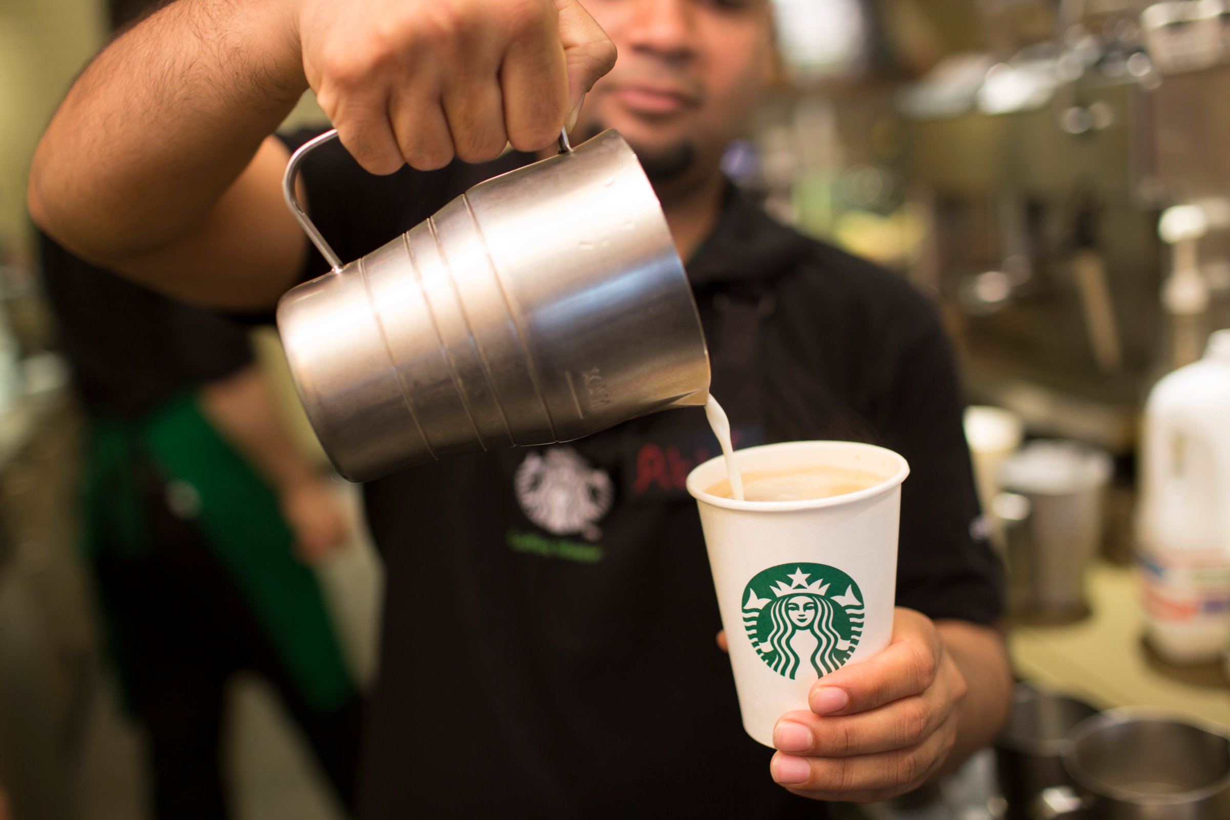 An employee pours milk into a cardboard coffee cup inside a Starbucks Corp. coffee shop in London on June 9, 2014.