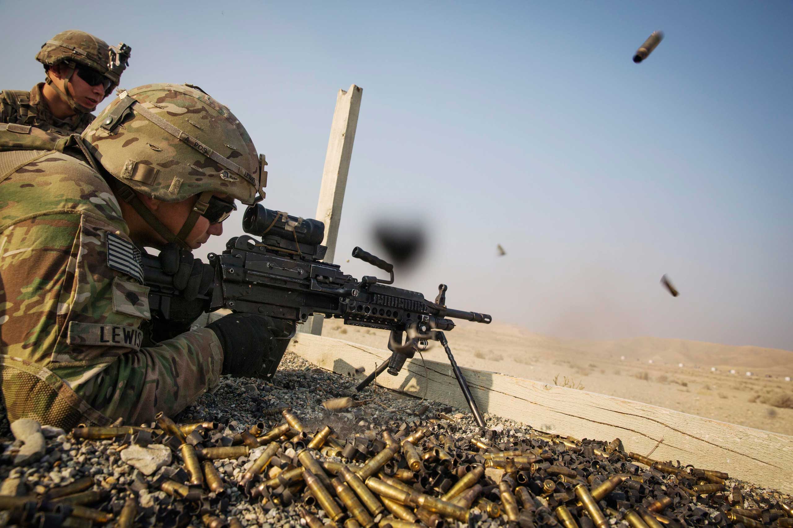 A U.S. soldier from the 3rd Cavalry Regiment is watched as he fires a squad automatic weapon during a training mission near forward operating base Gamberi, in the Laghman province of Afghanistan on Dec. 15, 2014.