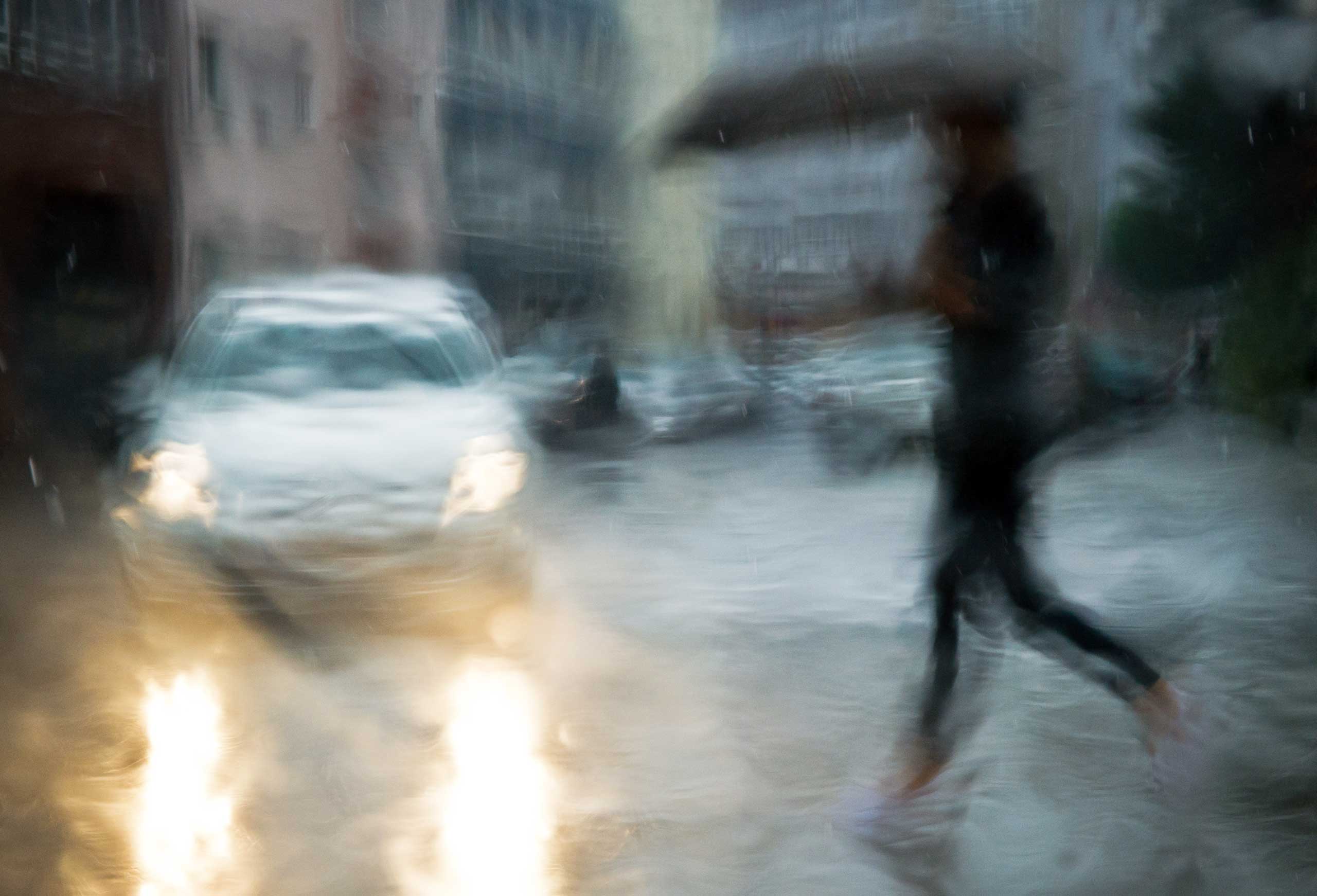 A woman with an umbrella crosses a street in Hanover, Germany,  Aug. 4, 2014. Photographed through the rain-wet window of a car.
