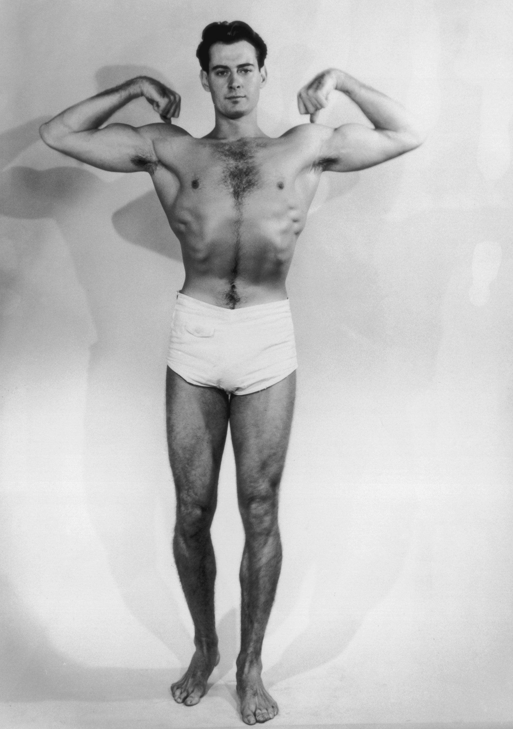 A muscular young man flexes his biceps, circa 1930.