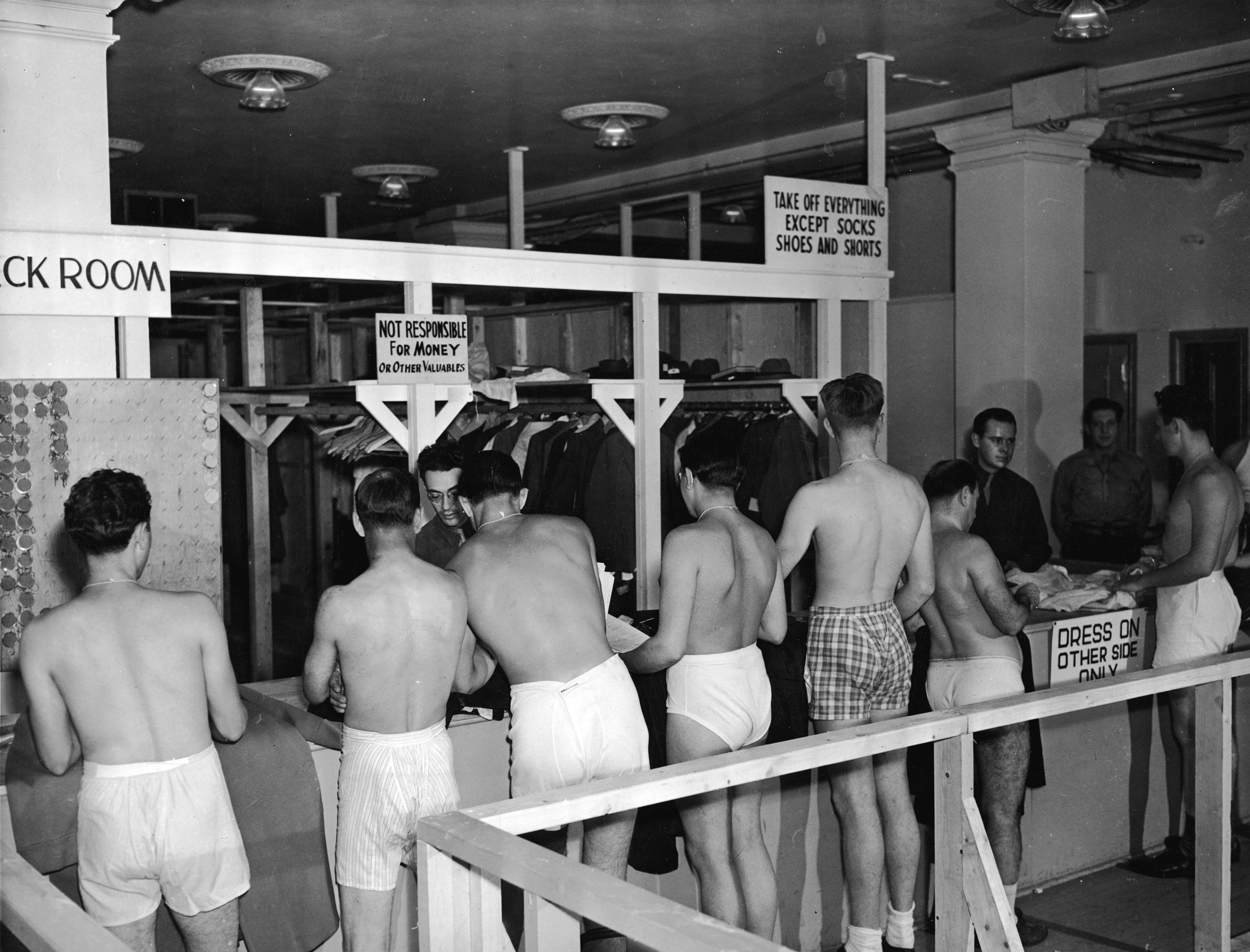 A line of underwear-clad draftees wait in line to check their clothes at an unidentified military facility, August 1944.