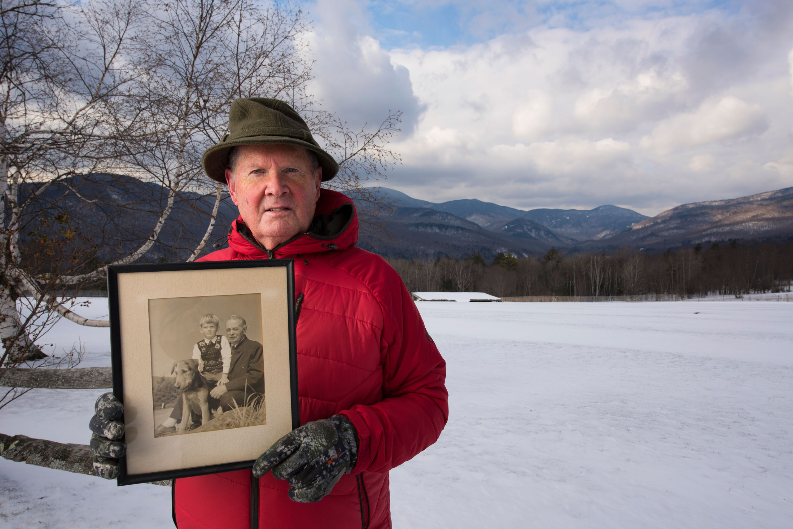 Portrait of Johannes von Trapp at the Trapp Family Lodge, alongside a field where music is performed in warmer weather. He is holding a portrait of his father and himself. (Joe McNally for LIFE)