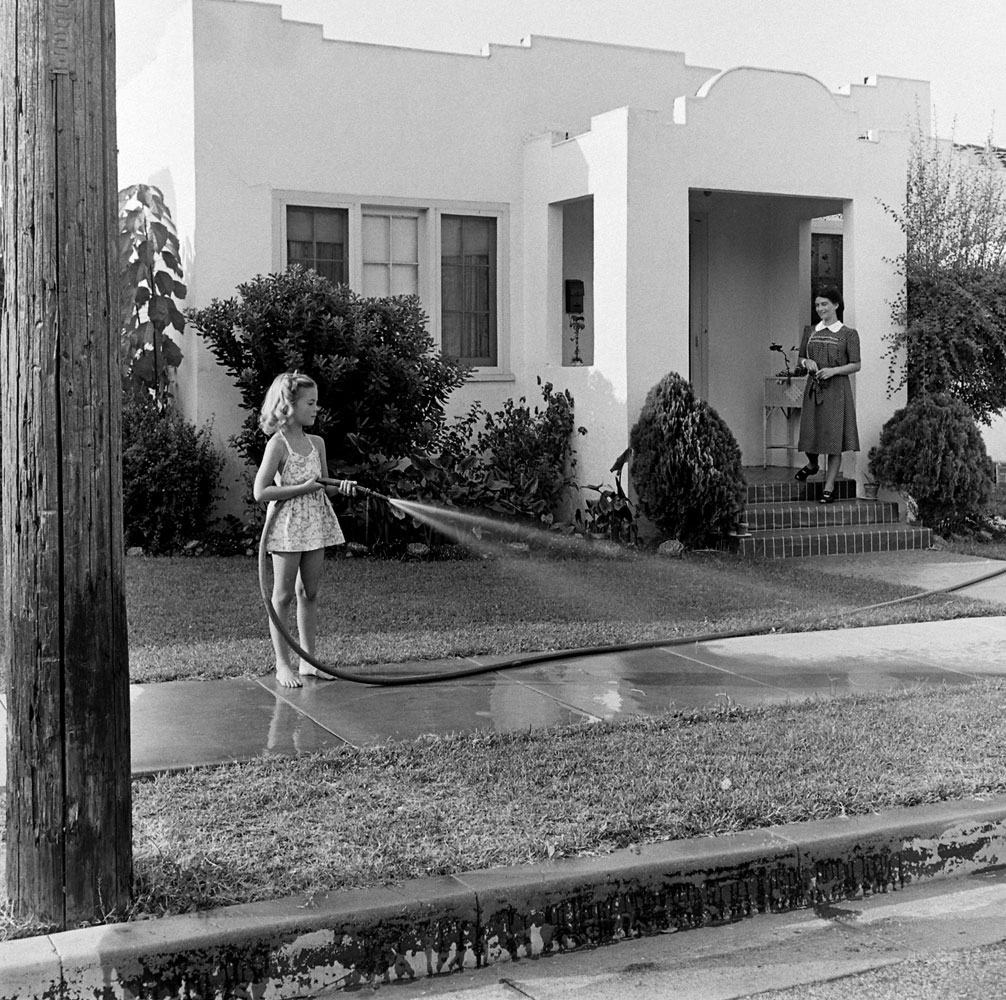 Natalie Woods waters the lawn as her mother, Maria Gurdin, supervises