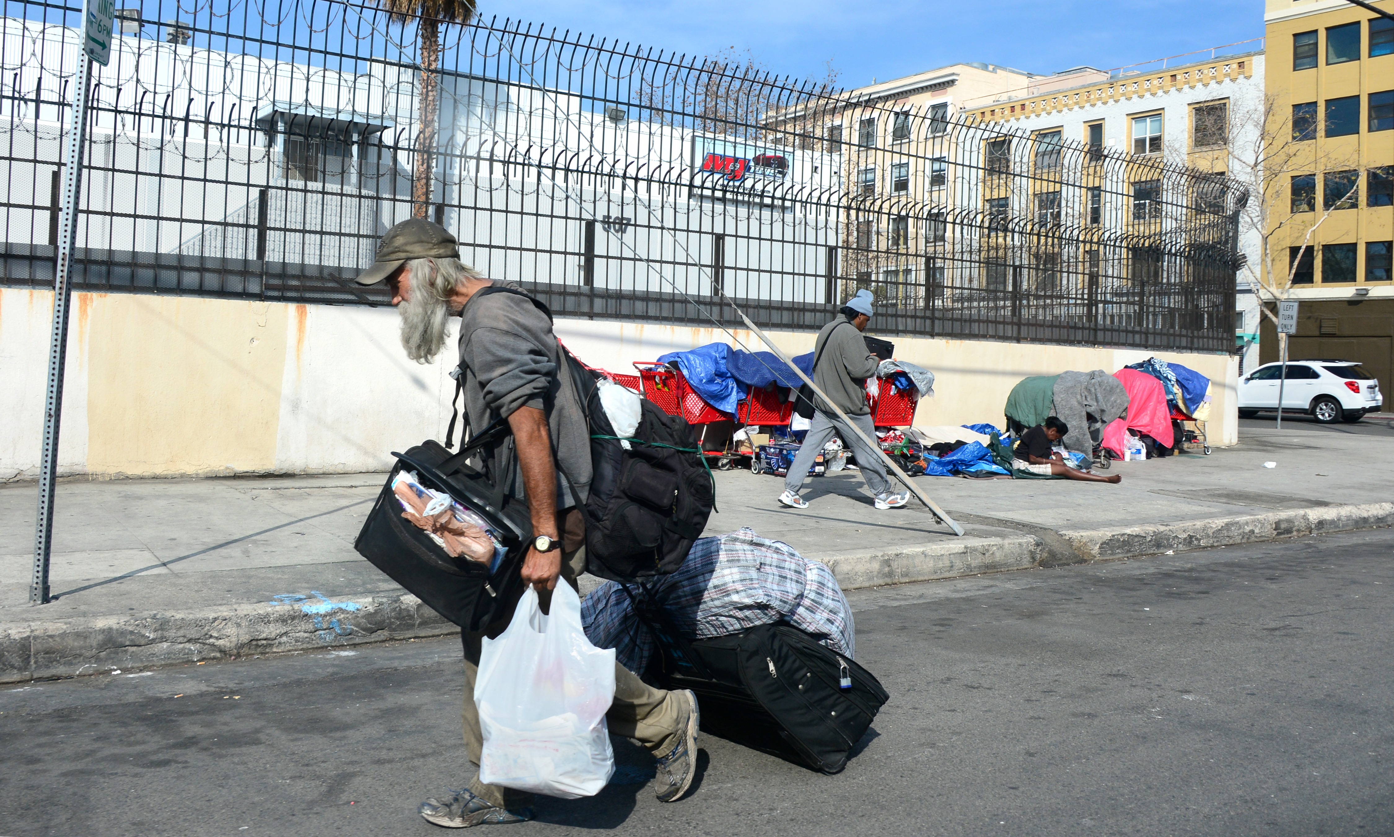 A man carries his belongings while walking past homeless people sitting amid their belongings on a street in downtown Los Angeles, California, on January 8, 2014. (FREDERIC J. BROWN—AFP/Getty Images)
