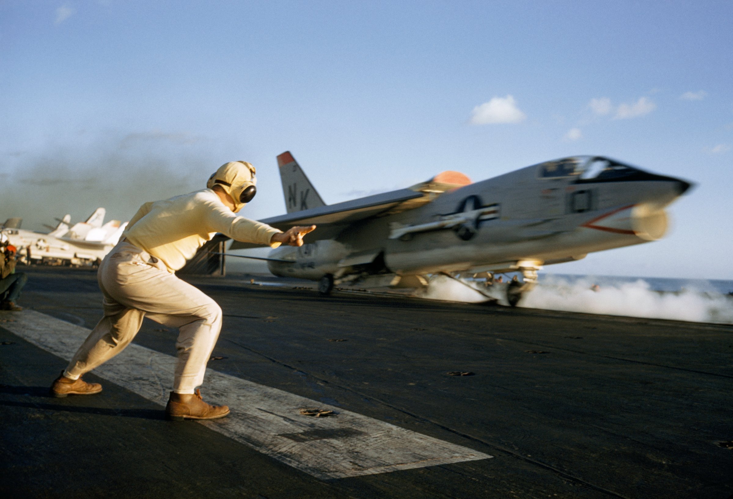 An officer guides a Crusader aircraft at launch on USS Ranger's deck, Pacific Ocean
