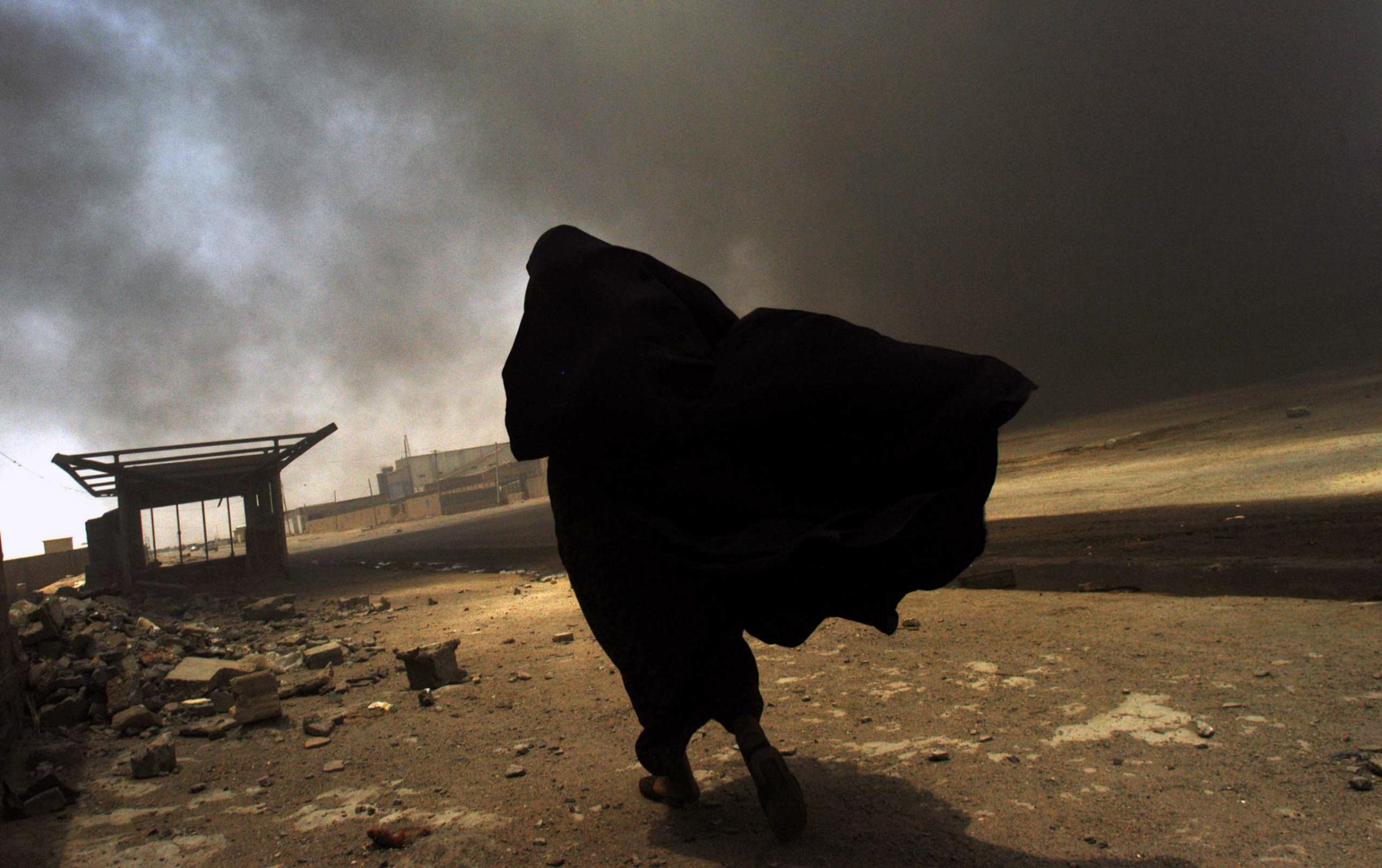 BASRA, IRAQ - MAY 26: An Iraqi woman walks through a plume of smoke rising from a massive fire at a liquid gas factory as she searches for her husband in the vicinity of the fire in Basra, Iraq, May 26, 2003.  The fire was allegedly started by looters picking through the factory, and residents in the vicinity feared the explosion of the four liquid gas tanks on the premisis.  Weeks after the end of the war, looting continues to be one of the main problems for both Basra and Bagdad cities as coalition forces struggle to get life back to normal.  (Photo by Lynsey Addario/Getty Images Reportage)