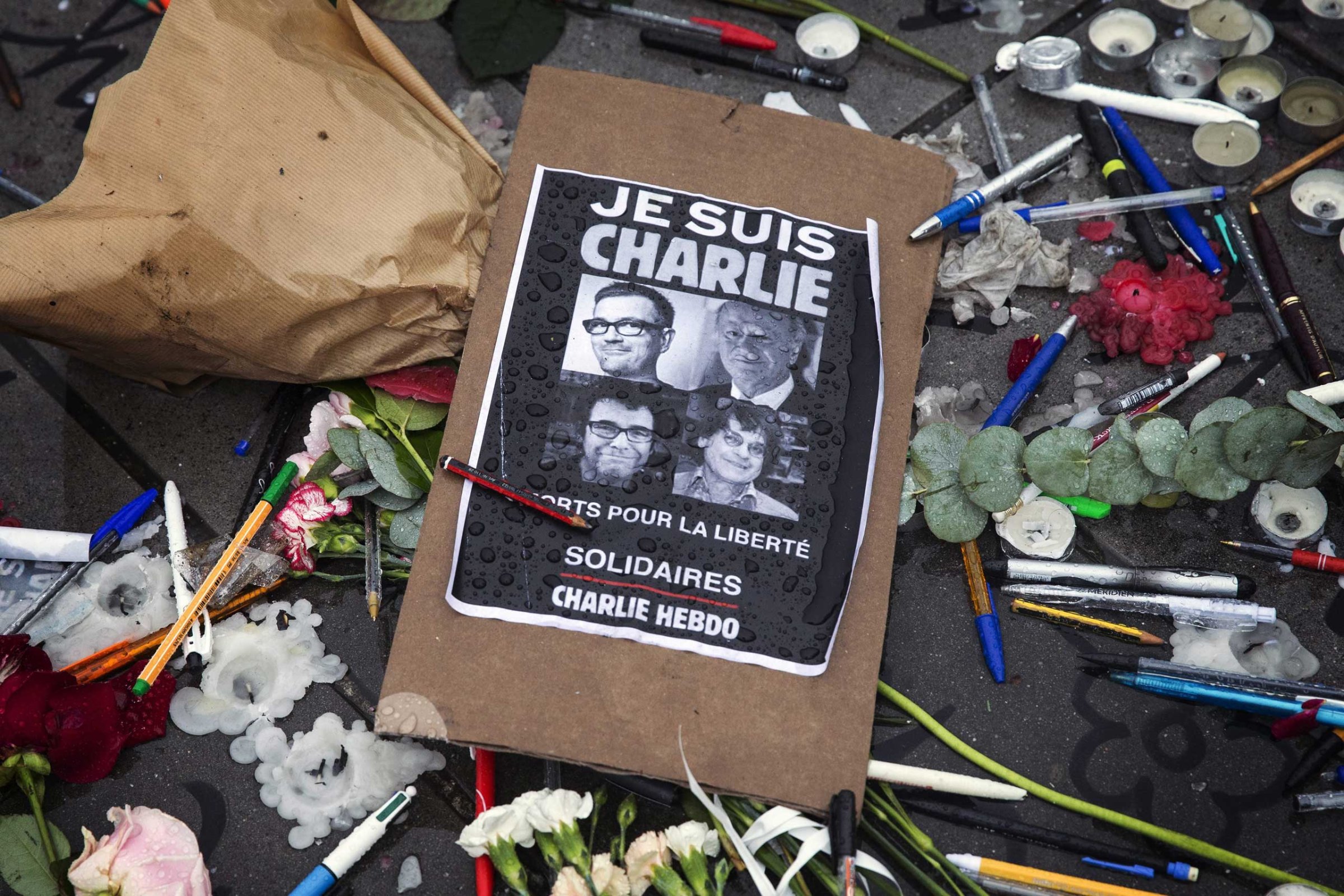 A poster reads 'Je suis Charlie' (I am Charlie) amid symbolic pens and pencils on Place de la Republique as people gather for a minute of silence commemorating those killed in a shooting at French satirical magazine 'Charlie Hebdo', in Paris, Jan. 8, 2015.