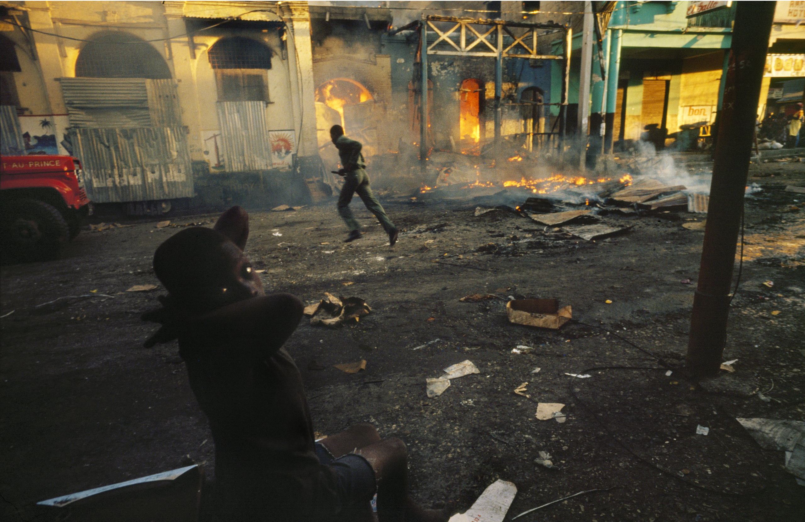Haitian fireman runs across street to burning buildings as a child
                              watches from a front row seat on election day in 
                              January 1988 in Pt-au-Prince, Haiti. Haitians set buildings on fire to protest against presidential elections they felt were
                              engineered by the Haitian military after elections two months earlier
                              were cancelled because of violence and massacres.
