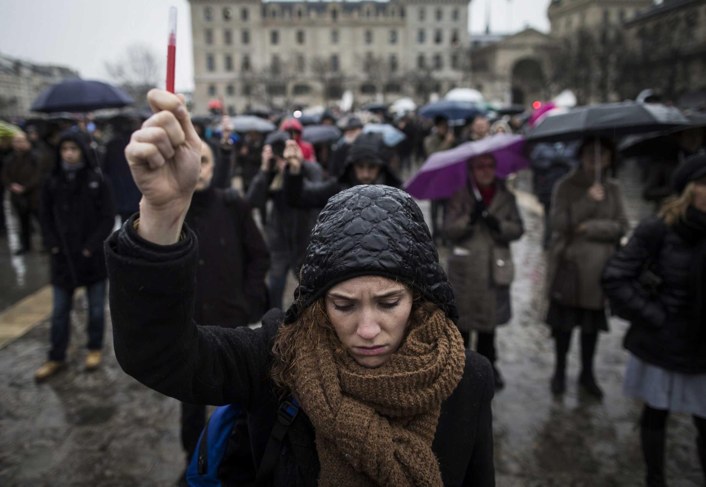 A young woman holds aloft a symbolic people as she joins others gathered for a minute of silence in front of Notre Dame cathedral, in Paris, Jan. 8, 2014.