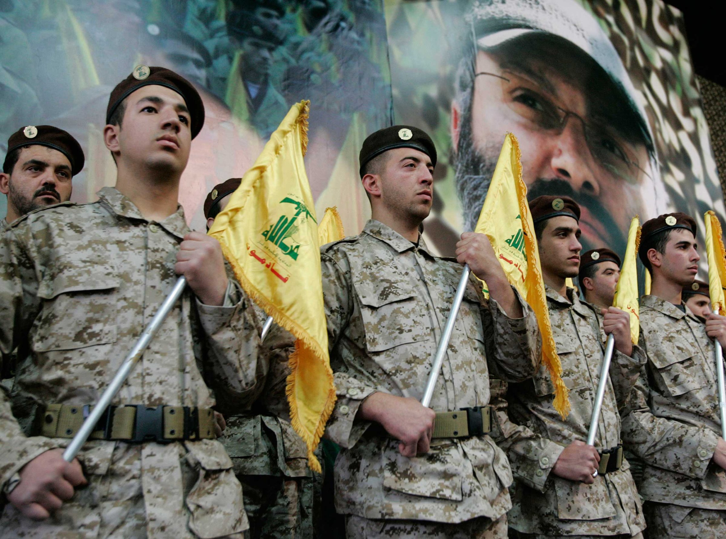 Hezbollah fighters hold their party flags and stand next to a portrait which shows their slain top commander Imad Mughniyeh, as they attend a rally to commemorate Mughniyeh and two other leaders, Abbas Musawi and Ragheb Harb, in the Shiite suburb of Beirut, Feb. 22, 2008.
