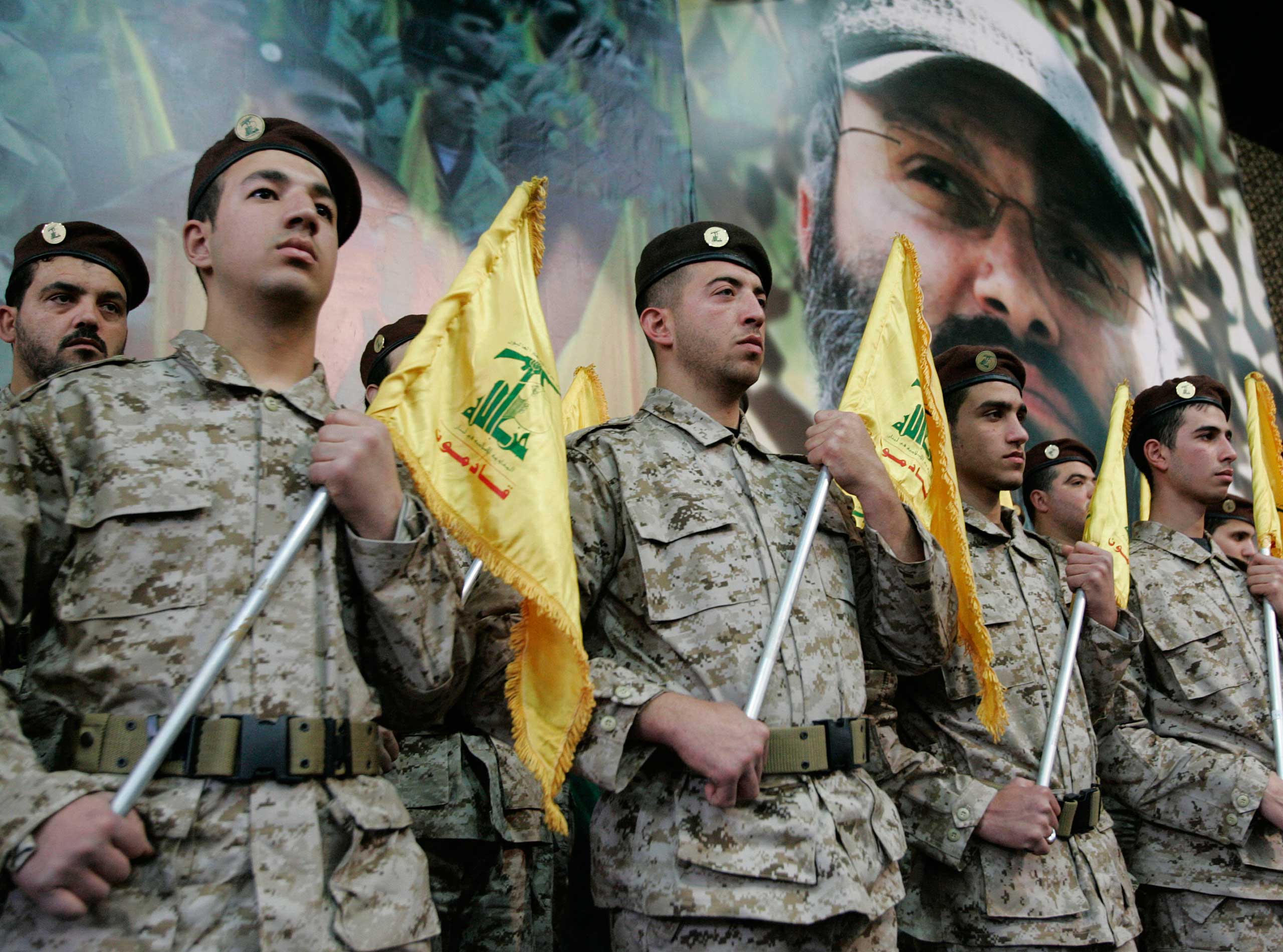 Hezbollah fighters hold their party flags and  stand next to a portrait which shows their slain top commander Imad Mughniyeh, as they attend a rally to commemorate Mughniyeh and two other leaders, Abbas Musawi and Ragheb Harb, in the Shiite suburb of Beirut, Feb. 22, 2008. (Hussein Malla—AP)