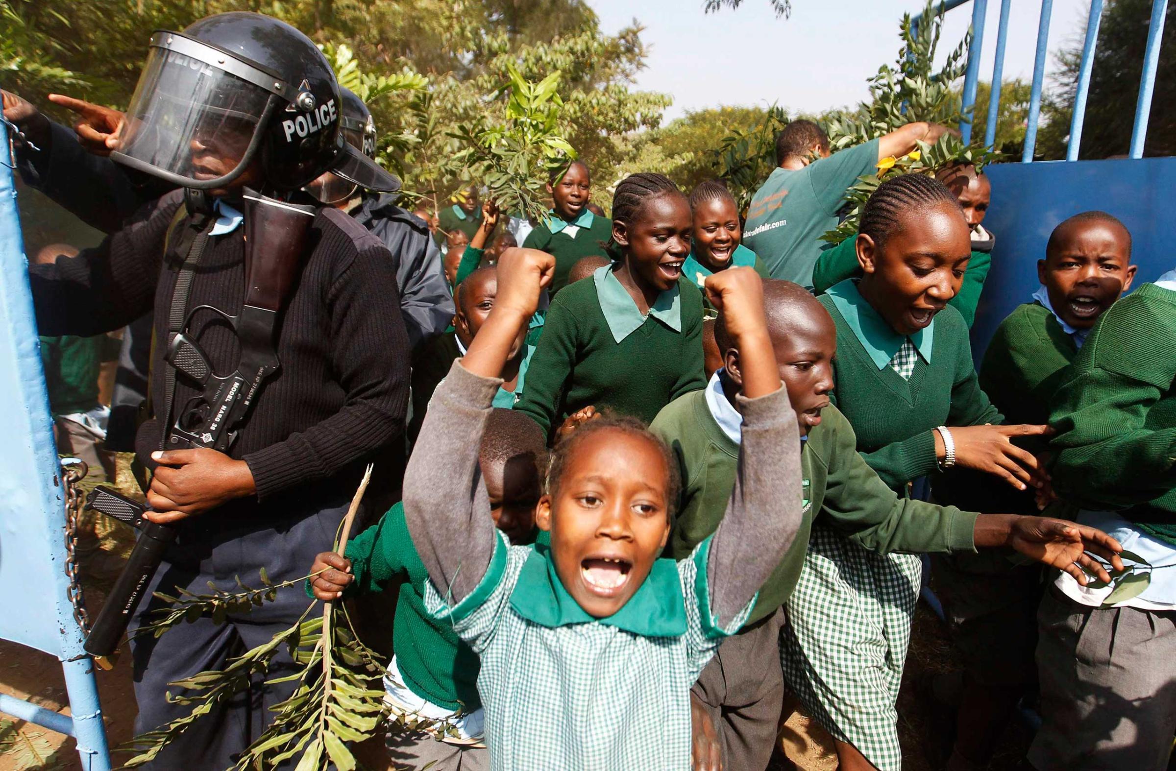 Students from Langata primary school run past riot police as they protest against a perimeter wall illegally erected by a private developer around their school playground in Nairobi, Jan. 19, 2015.