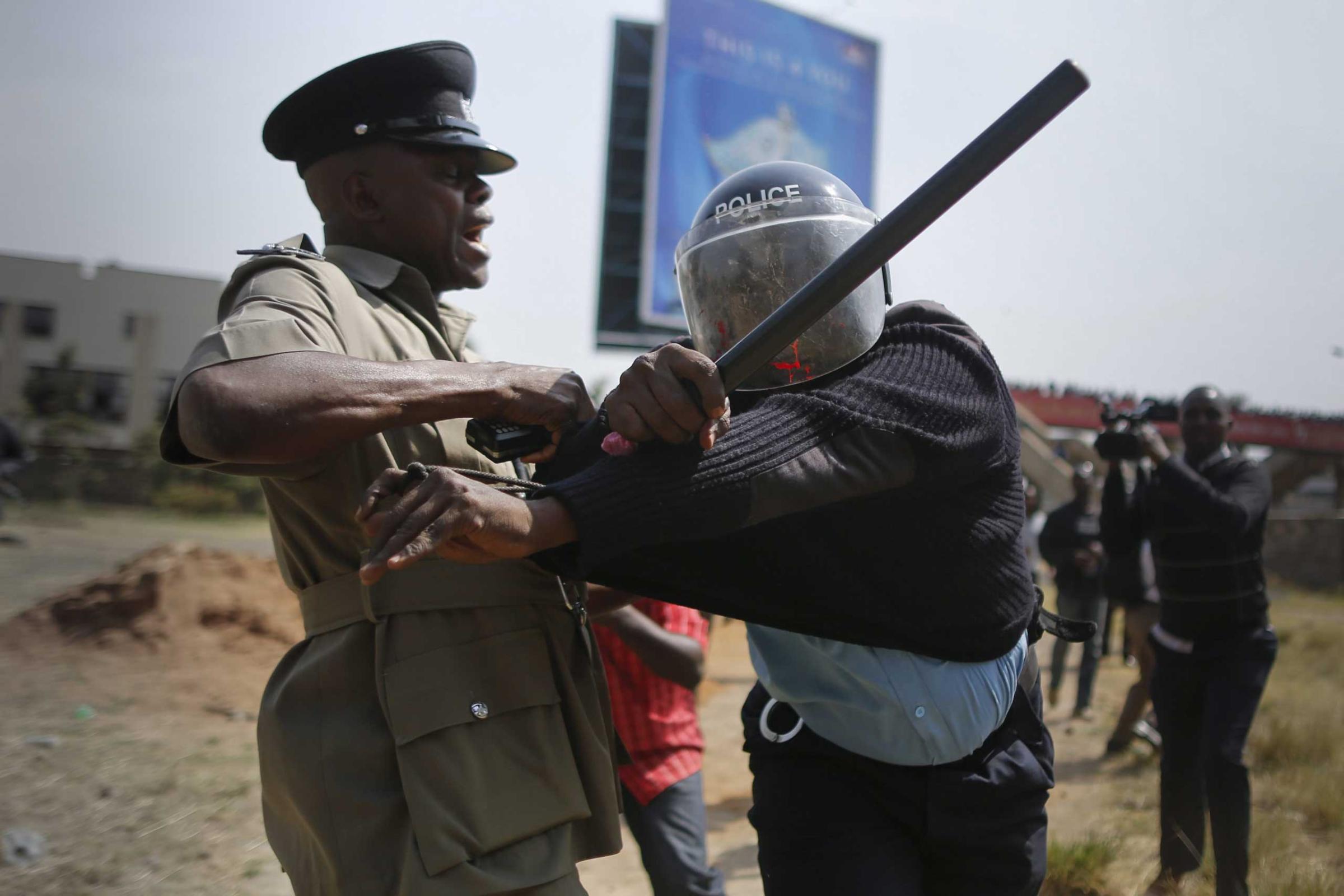 A police officer reacts as his colleague tries to calm him down after he was hit by a rock thrown by a protester during a protest against alleged land grabbing at Langata Road Primary School in Nairobi, Jan. 19, 2015.