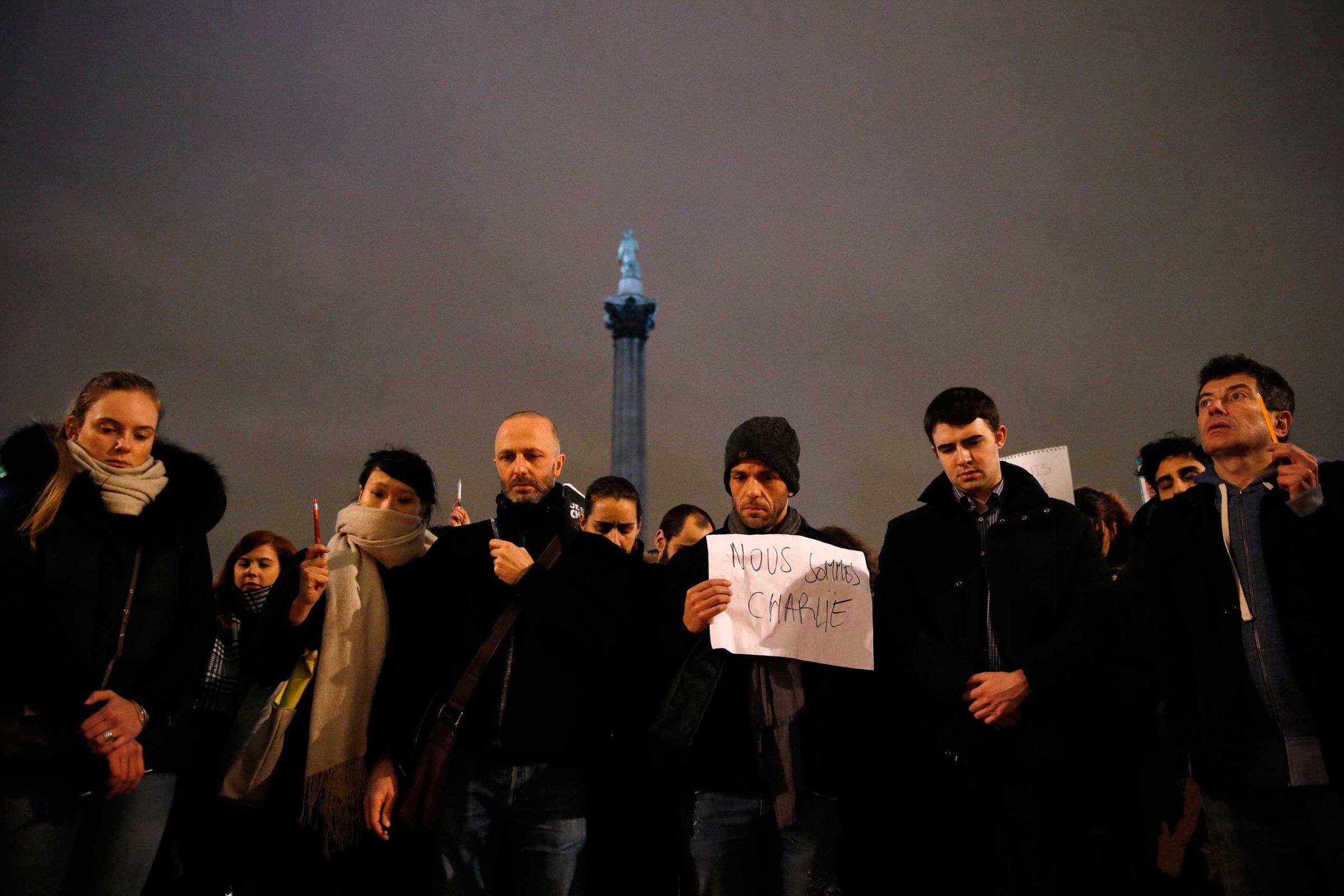 People raise pens and signs during a vigil to pay tribute to the victims of a shooting by gunmen at the offices of weekly satirical magazine Charlie Hebdo in Paris, at Trafalgar Square in London, Jan. 7, 2015.