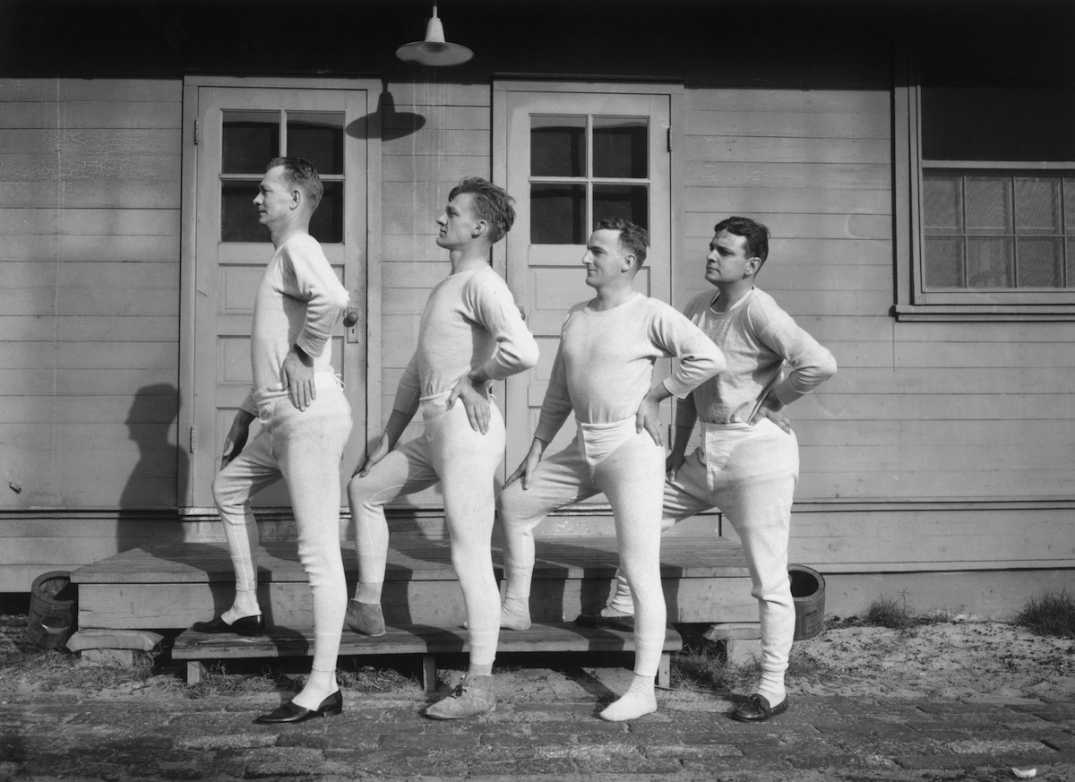 Four men wearing long underwear pose in a profile lineup, circa 1915.