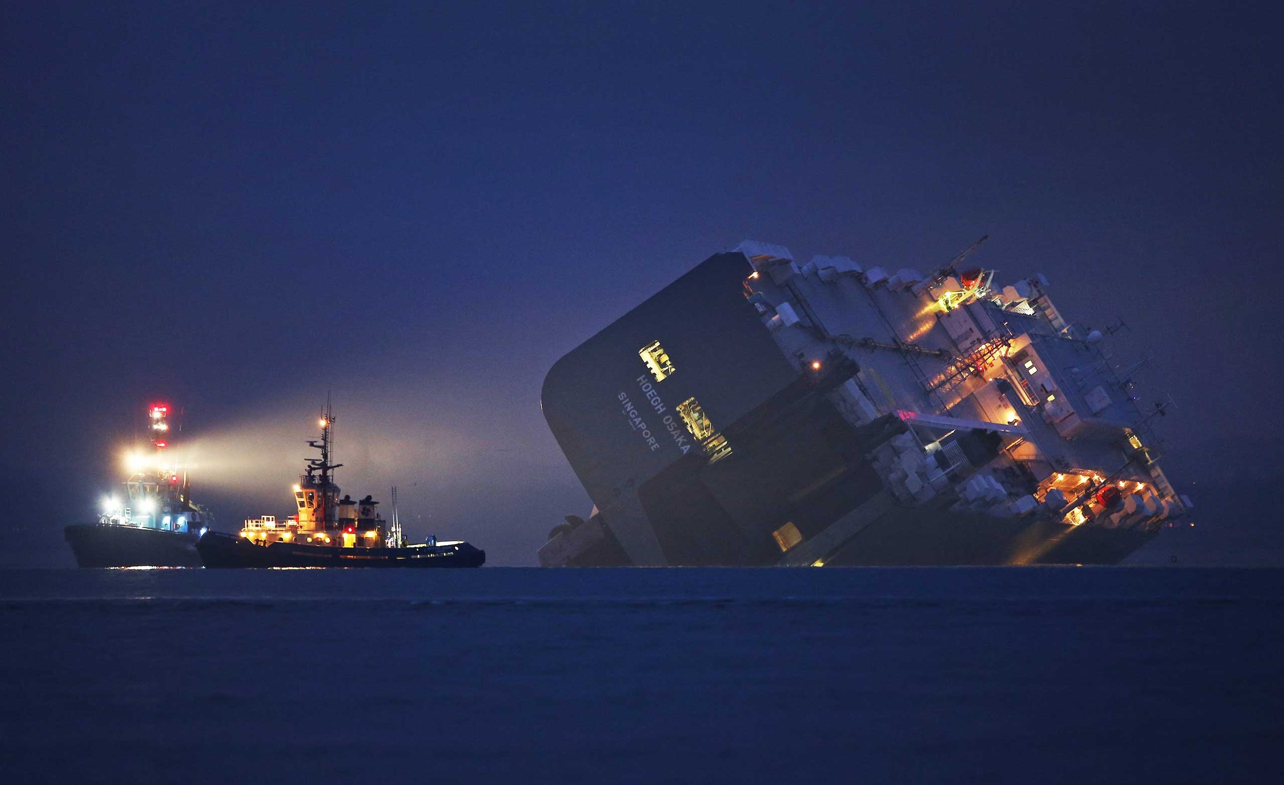 Jan 4. 2015.  A salvage tug lights the hull of the stricken Hoegh Osaka cargo ship after it ran aground on a sand bank  Cowes, England.