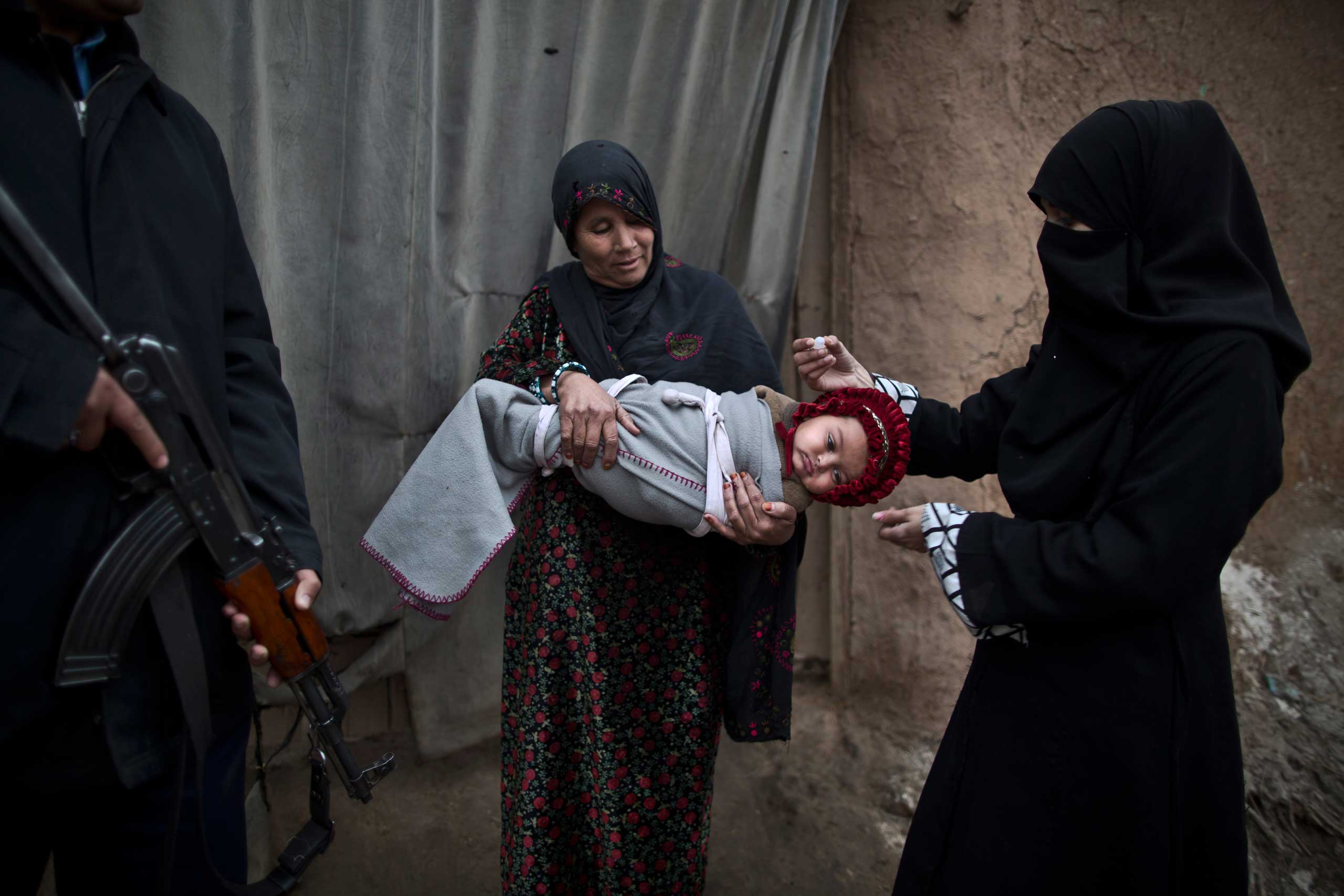 Jan. 21, 2015. A Pakistani police officer, left, stands guard while a polio worker vaccinates an Afghan refugee child in a slum on the outskirts of Islamabad, Pakistan. Militants have spread a rumor among ultraconservative parents in Pakistan's deeply religious northwest, claiming that the vaccine is a ploy by the West to limit the world’s Muslim population and will make their children impotent.