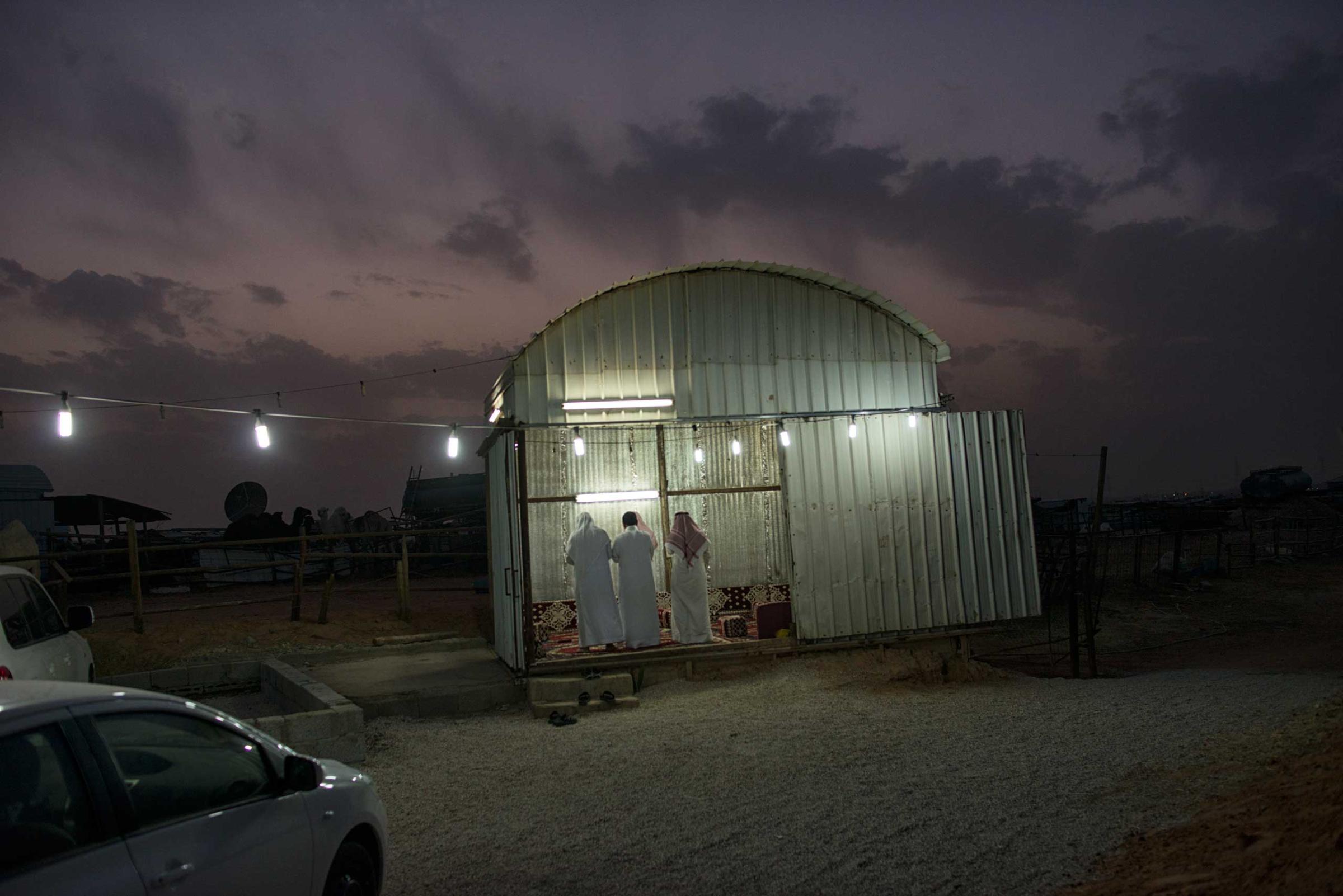 Saudi men pray at dusk at a camel market outside of Riyadh, Saudi Arabia, March 3, 2013.   Despite an extremely wealthy sector of society in Saudi Arabia, and the the veneer of widespread affluence projected outside the Kingdom, severe poverty is as much an aspect of life in Riyadh as wealth. (Credit: Lynsey Addario/ VII)