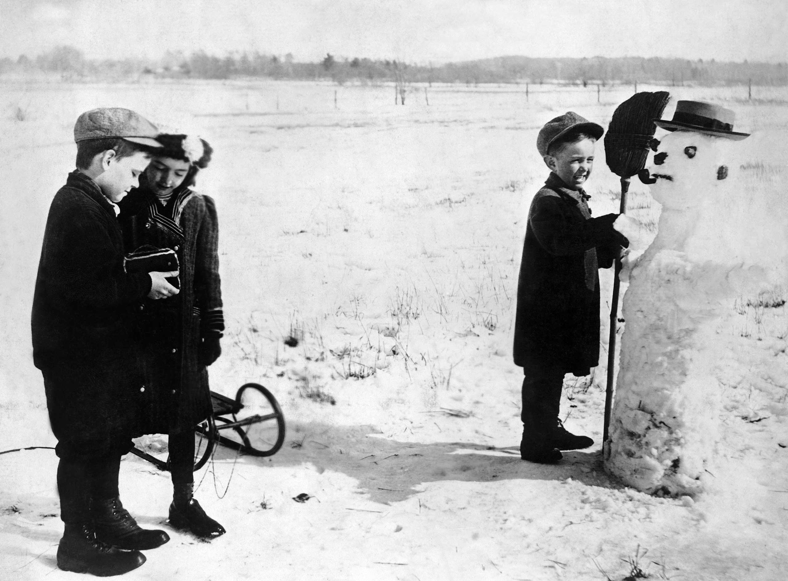Children take a photo with their snowman, circa 1930s