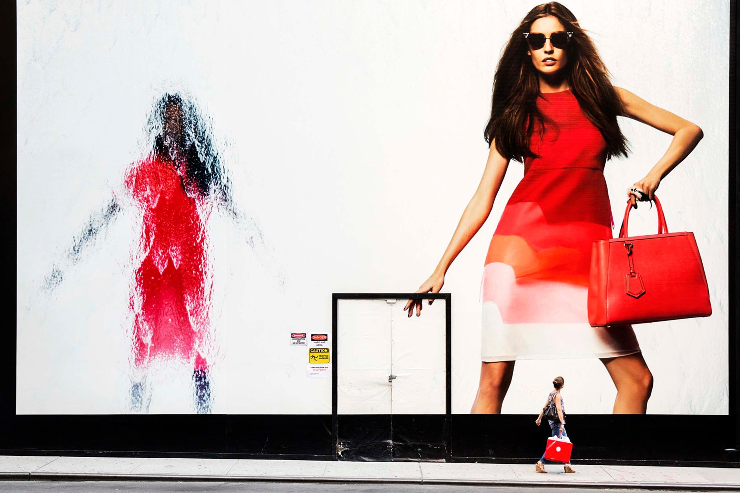 A woman holding a red shopping bag passes by a Fendi billboard on Madison Avenue, New York, June 21, 2014.