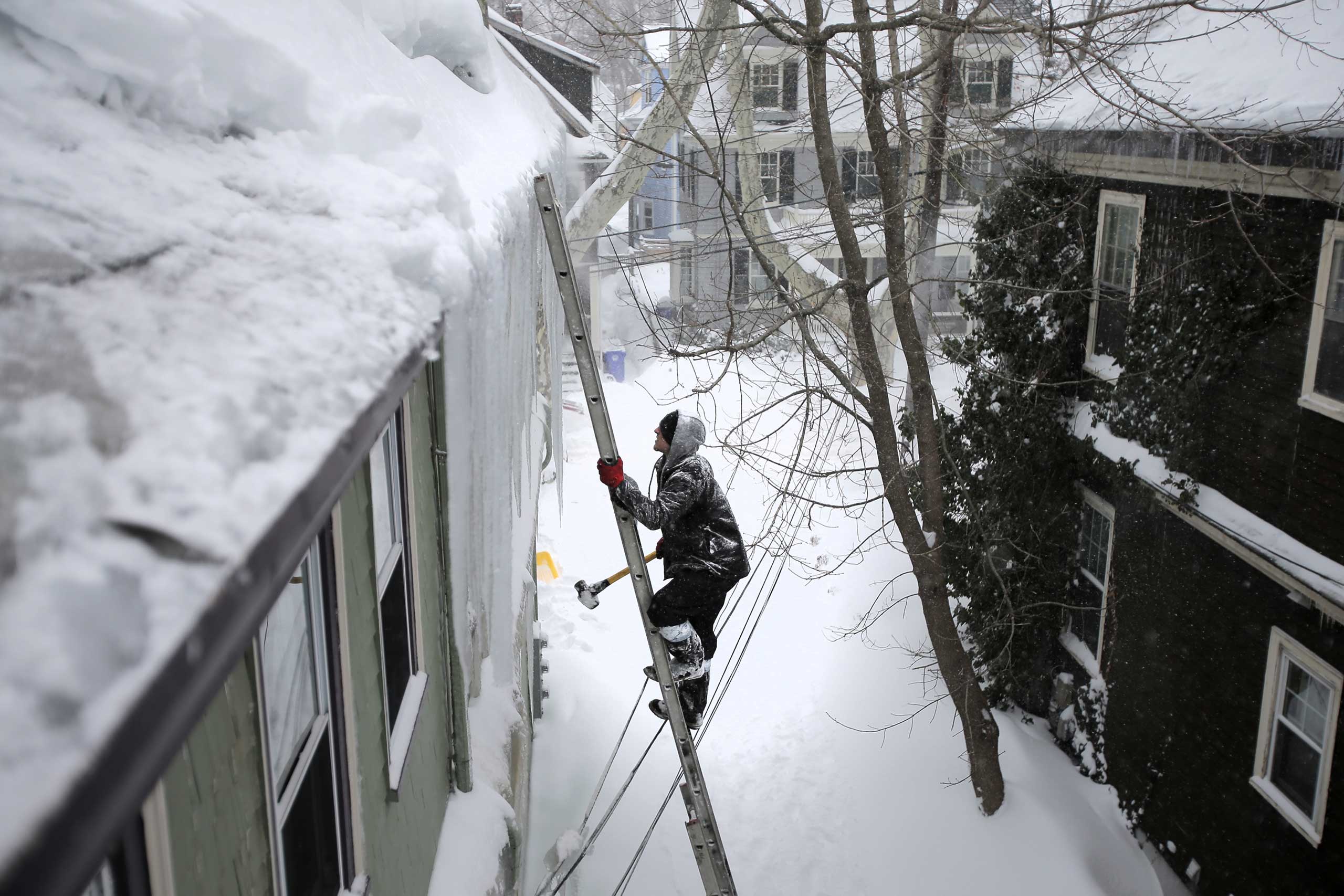 Jay Bullens Jr. of Able Roofing climbs with a sledgehammer to the third floor of a house to knock snow and ice from a roof on Beals Street in Brookline, Mass. on Feb. 9, 2015.