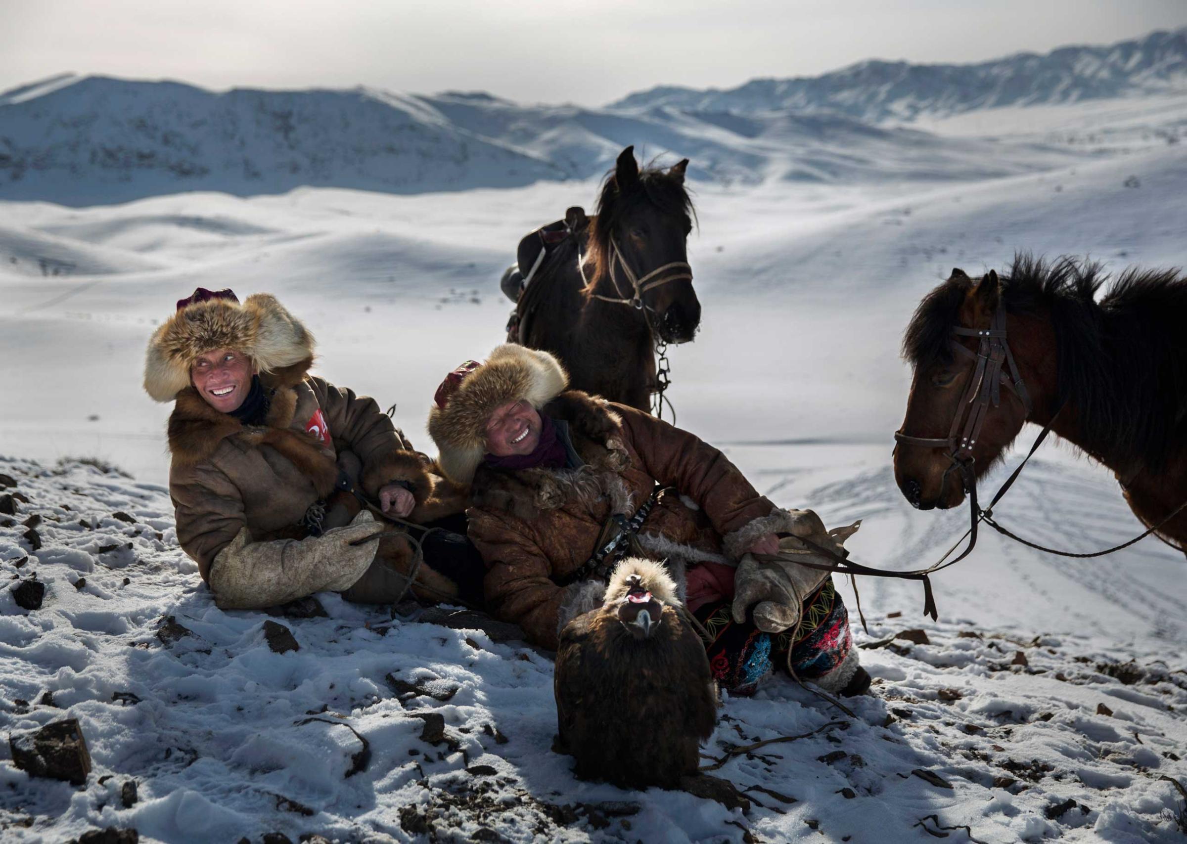 Chinese Kazakh eagle hunters laugh together as they rest during a local competition.