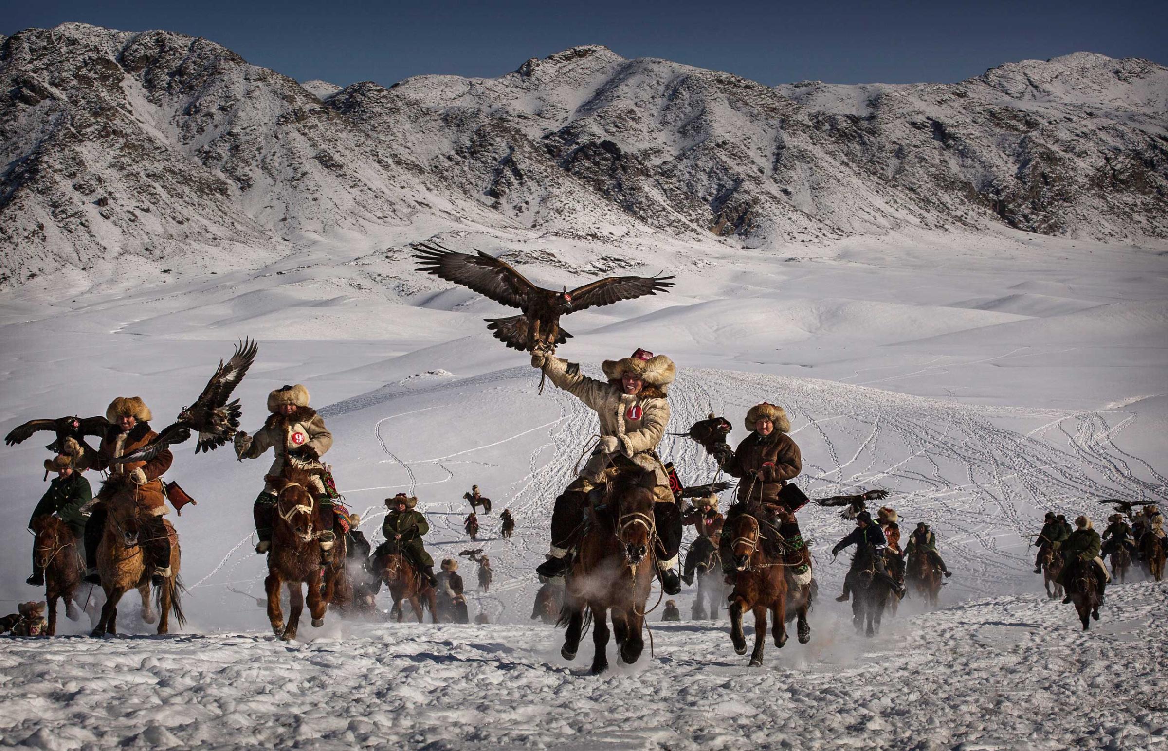 Chinese Kazakh eagle hunters ride with their eagles during a local competition.