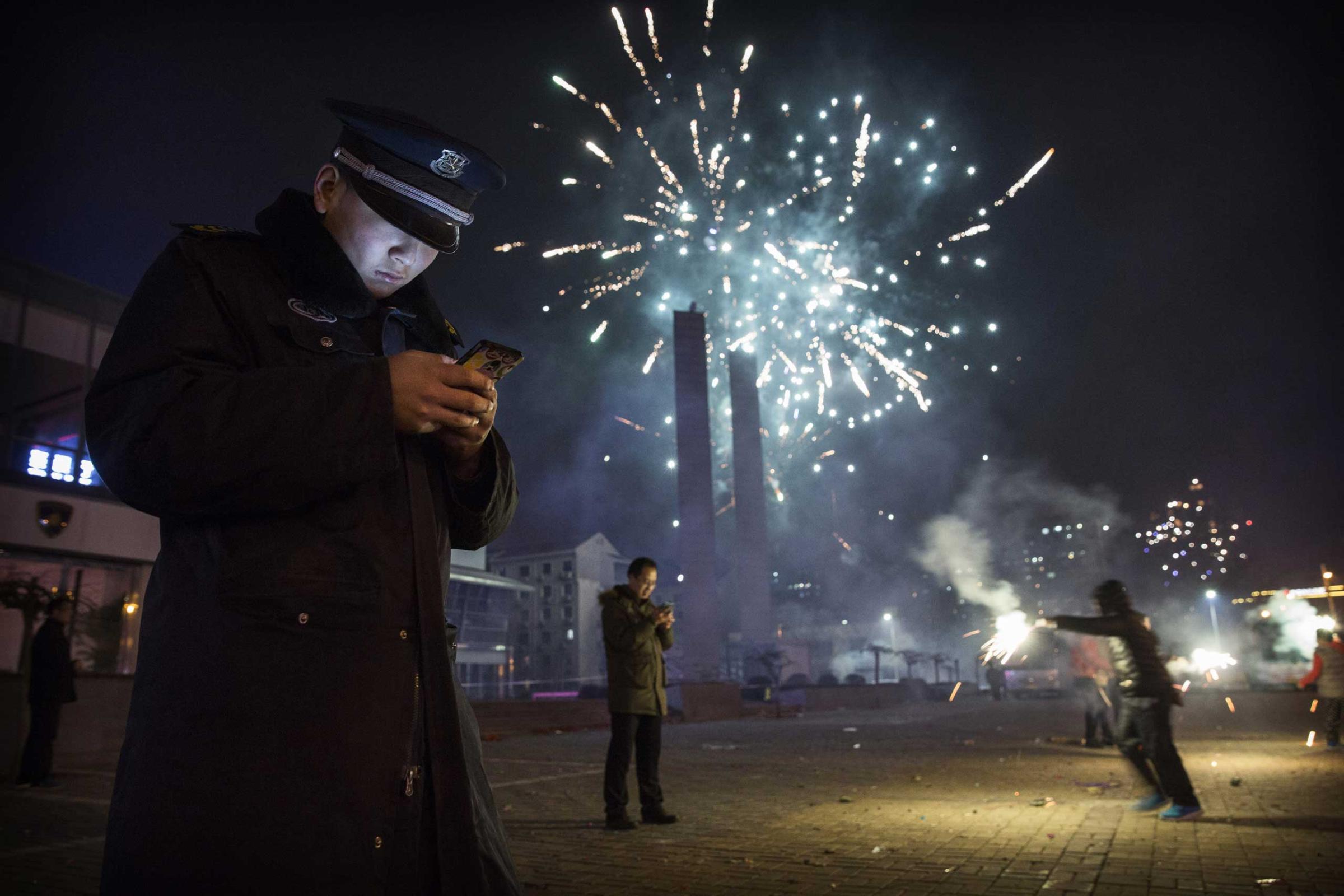 A Chinese security guard checks his smartphone as fireworks explode during celebrations of the Lunar New early on Feb. 19, 2015 in Beijing.