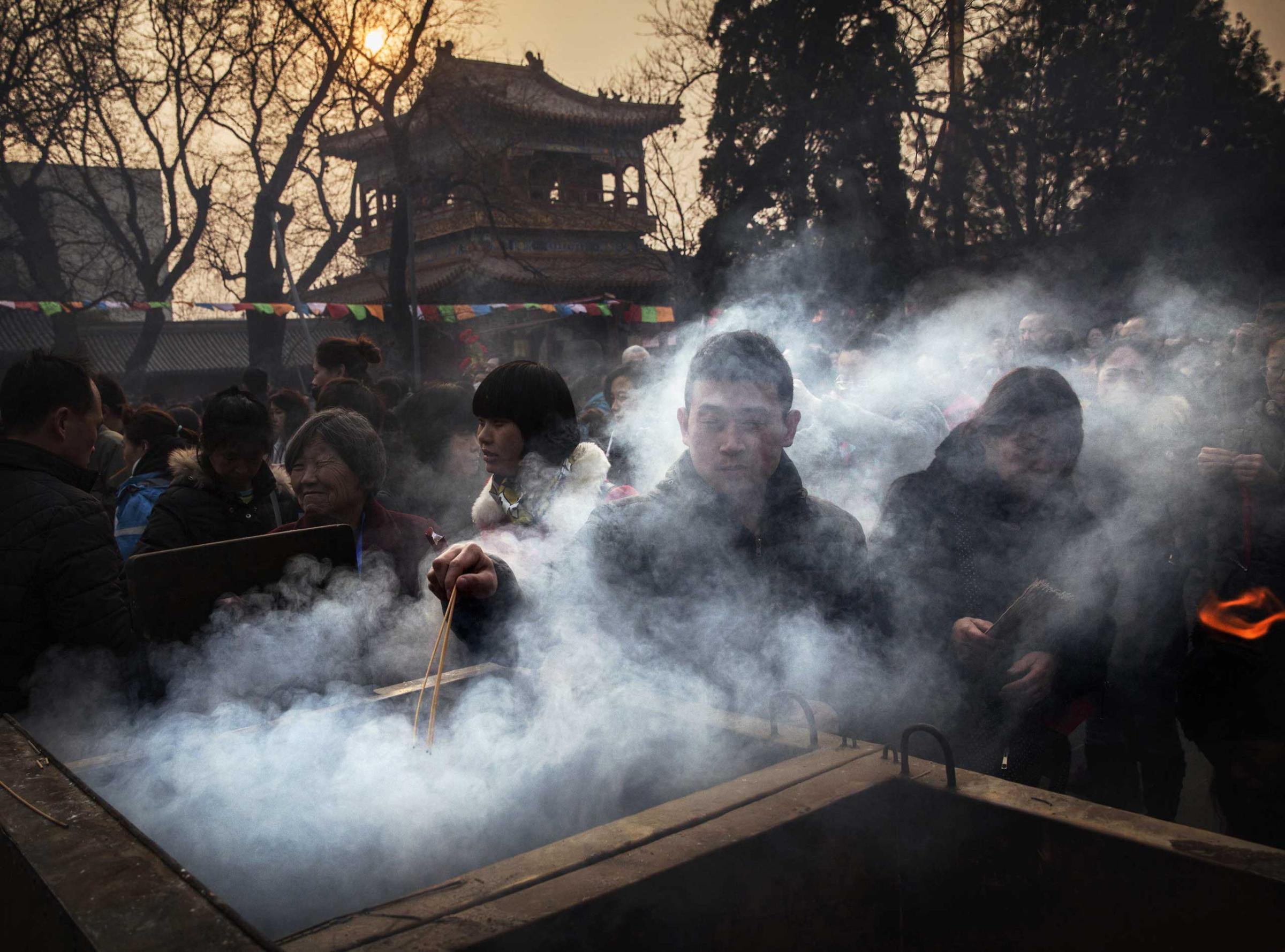 A Chinese man is shrouded in smoke from incense as he lights a stick while praying with others at the Yonghegong Lama Temple during celebrations for the Lunar New Year Feb. 19, 2015 in Beijing.
