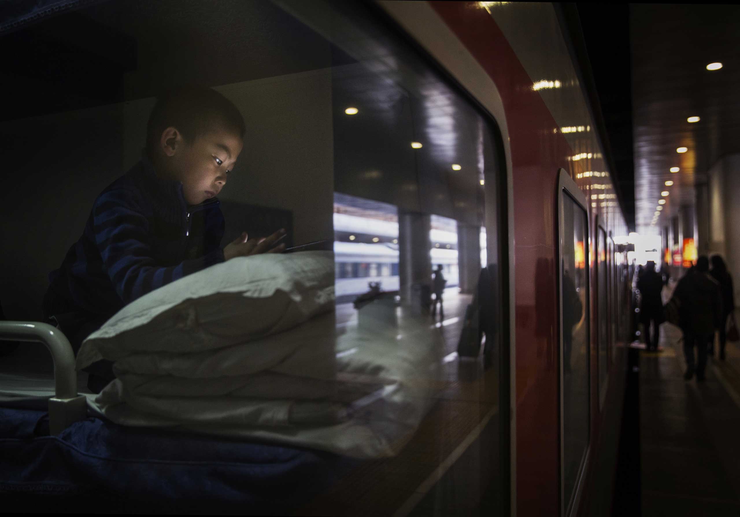 A boy uses a portable device as he lays in a sleeper on a train before leaving for the  Spring Festival at a local railway station on Feb. 17, 2015 in Beijing.