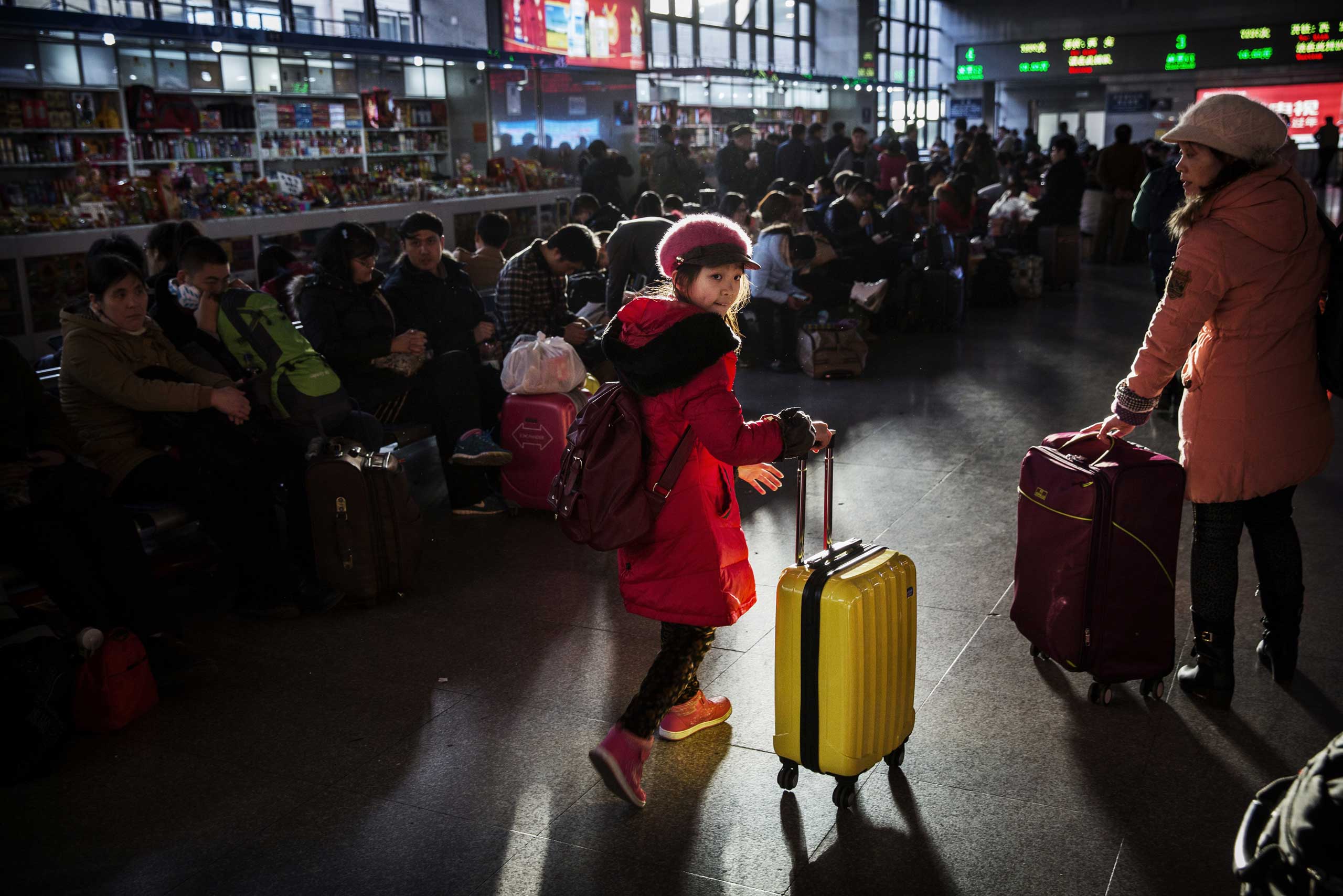 A young traveler wheels her bag as others wait in the departure area for a train at a local railway station on Feb. 16, 2015 in Beijing.