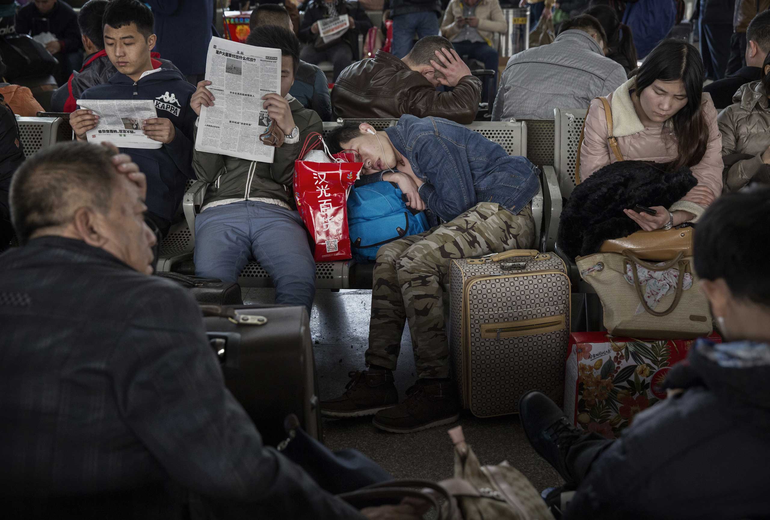 A traveler sleeps as others read and relax as they wait to leave for the  Spring Festival at a local railway station on Feb. 17, 2015 in Beijing.