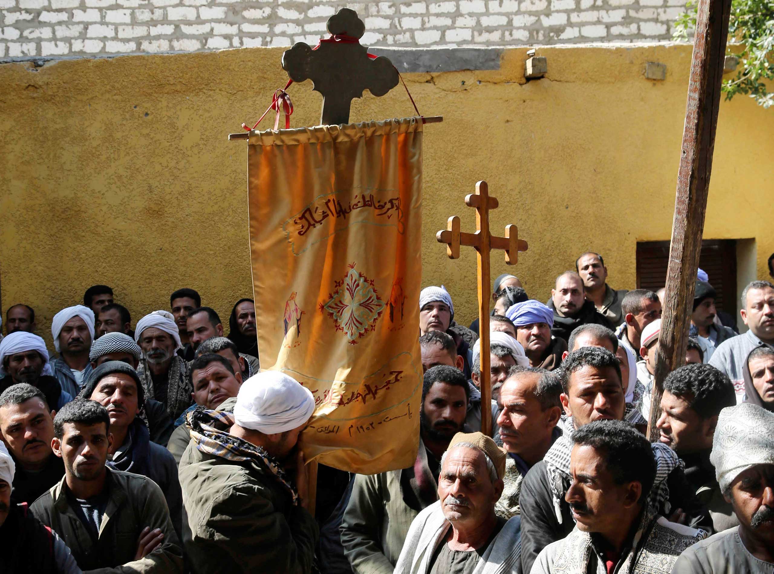 A Coptic man kisses a prayer banner, which is hung on a cross, as neighbors and friends of the relatives of Egyptian Coptic men who were killed in Libya stand at the courtyard of a church before attending a mass in Al-Our village, in Minya governorate, south of Cairo, Feb. 16, 2015.