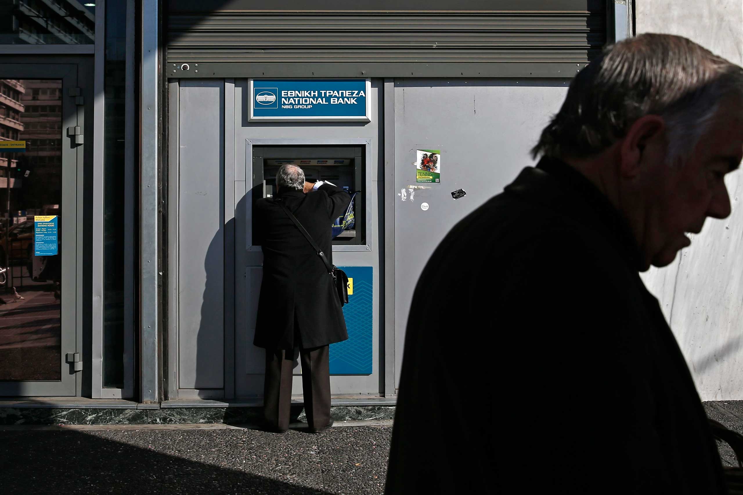 A man makes a transaction at an ATM outside a National Bank of Greece branch