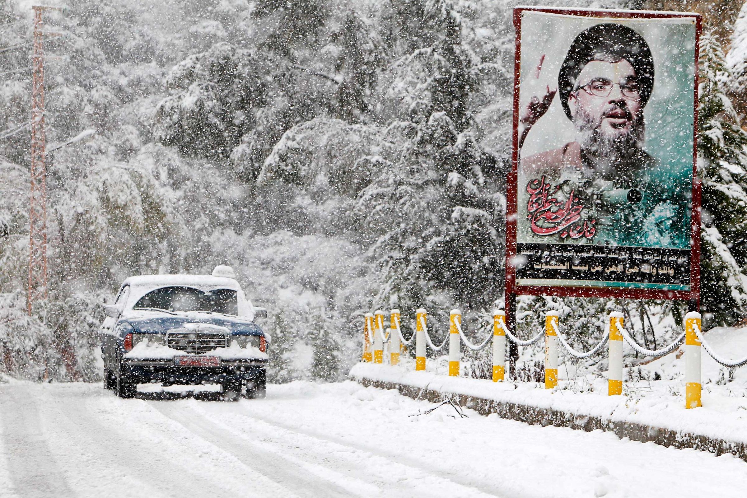 A snow covered taxi drives past a picture of Lebanon's Hezbollah leader Sayyed Hasan Nasrallah in Jbaa village, south Lebanon, Feb. 20, 2015.