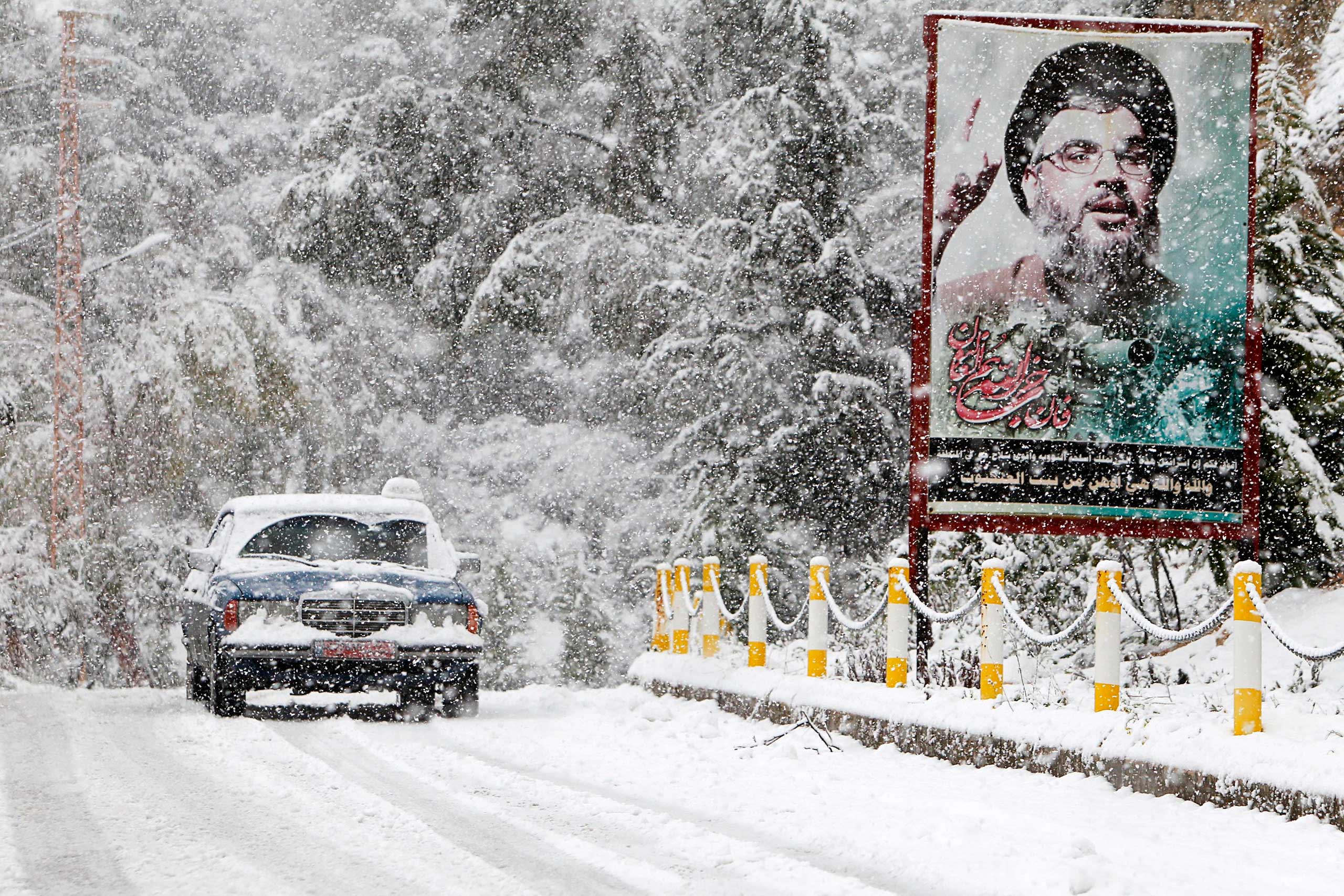 A snow covered taxi drives past a picture of Lebanon's Hezbollah leader Sayyed Hasan Nasrallah in Jbaa village, south Lebanon