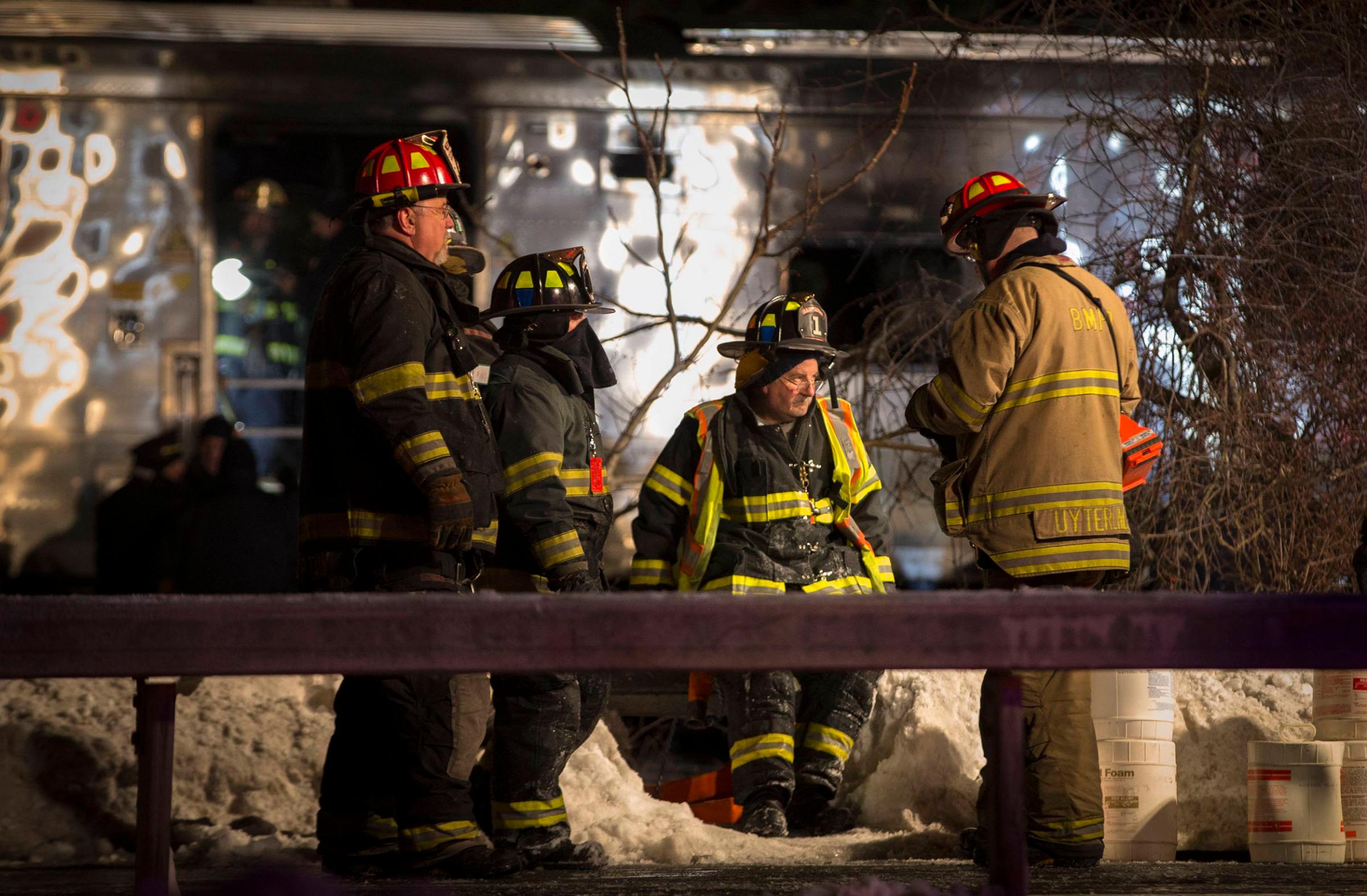 Firefighters and Emergency workers stand near a burnt Metropolitan Transportation Authority Metro North Railroad commuter train car near the town of Valhalla