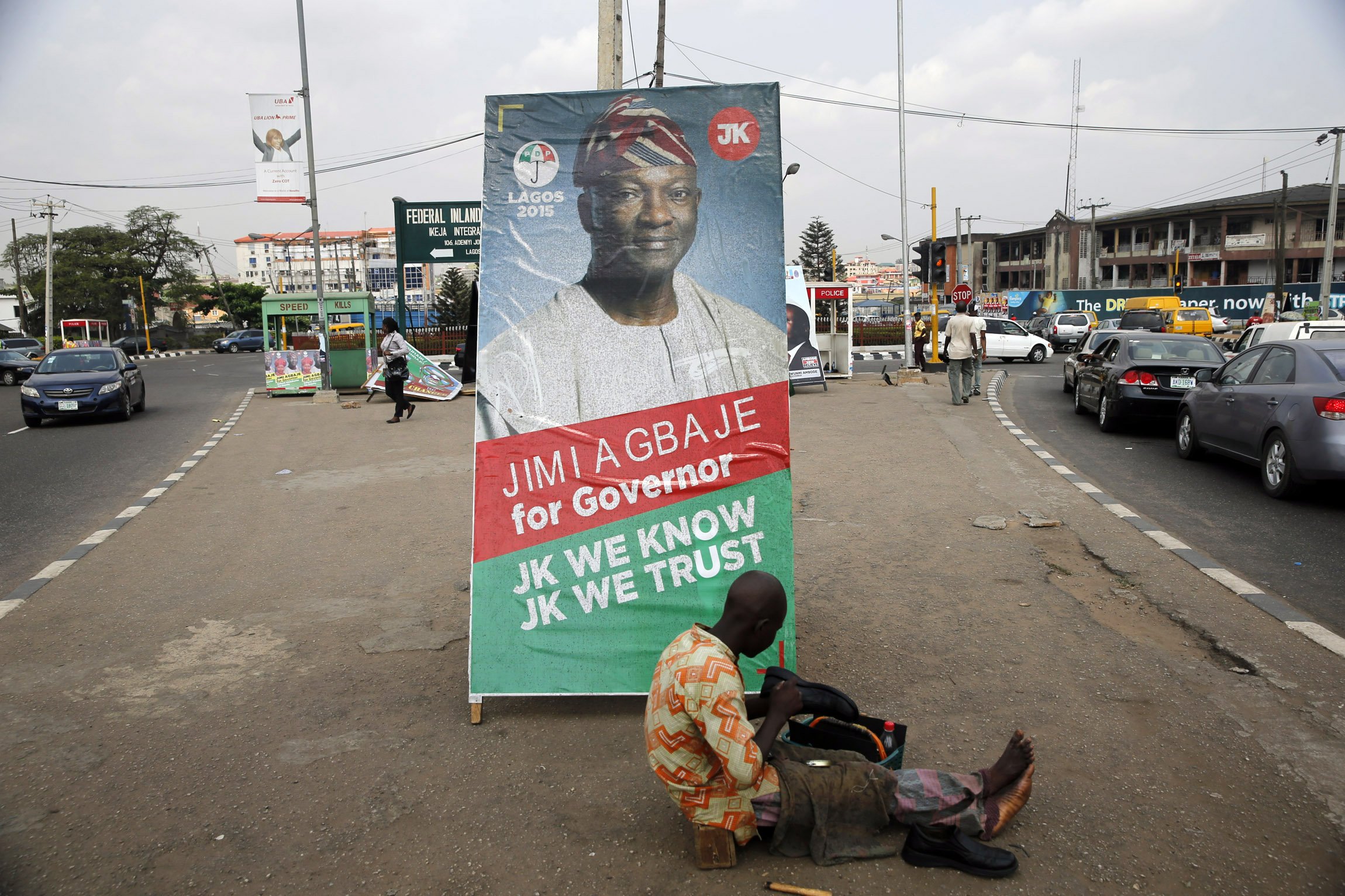 A shoe-mender works near a poster campaigning for Jimi Agbaje, along a road in the Ikeja district in Lagos
