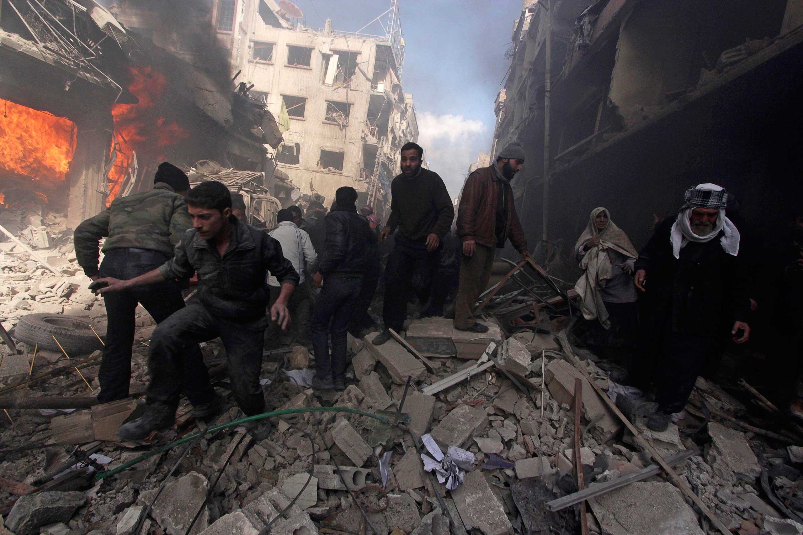 Feb. 9, 2015. People walk on rubble as others try to put out a fire after what activists said were airstrikes followed by shelling by forces loyal to Syria's President Bashar al-Assad in the Douma neighborhood of Damascus.