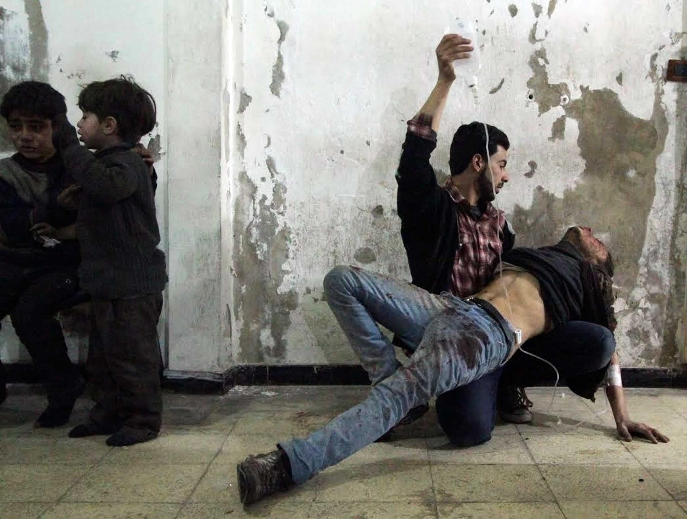 Man gives medical assistance to an injured man as two wounded children wait nearby at a field hospital after what activists said was an air strike by forces of Syria's President Assad in Damascus
