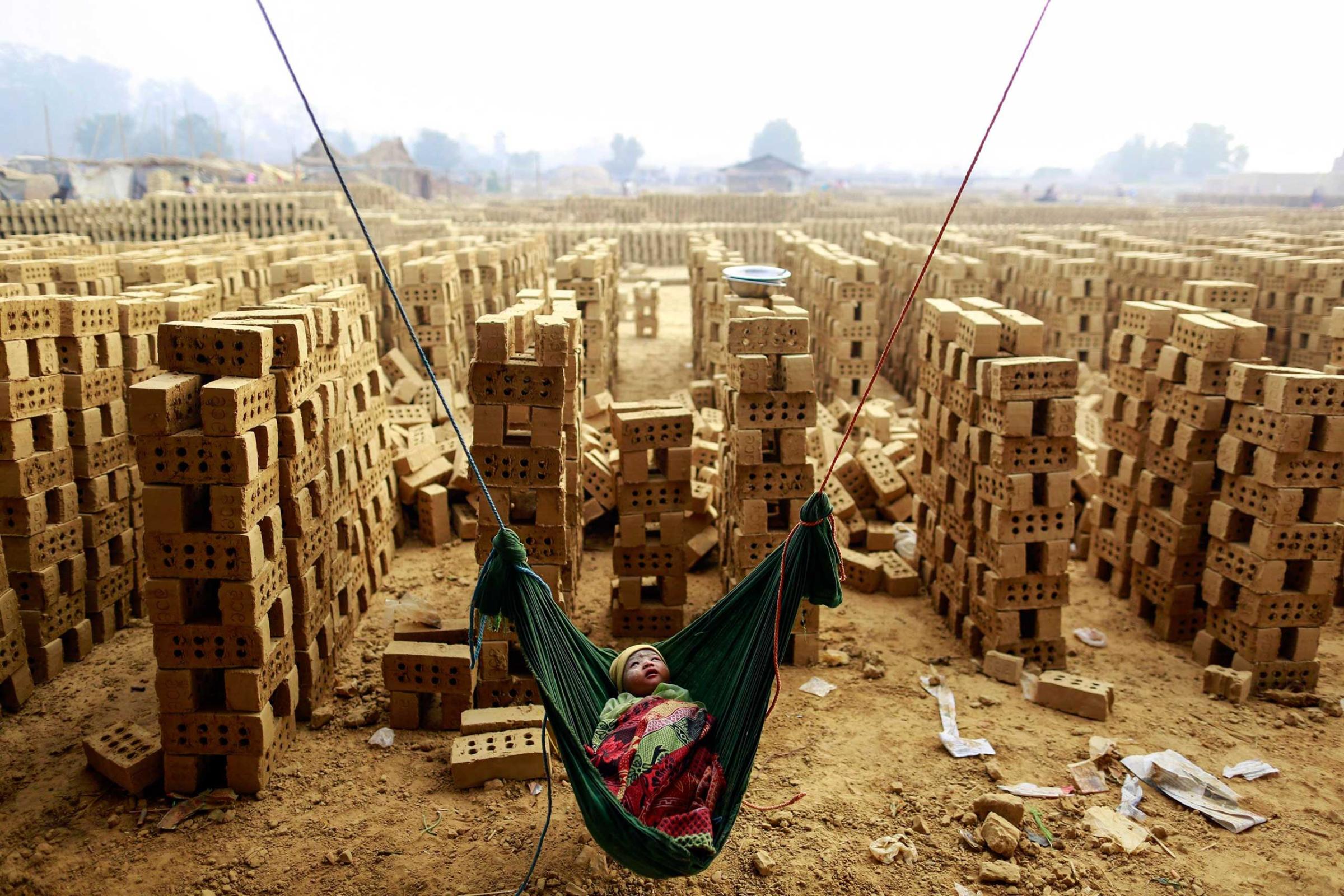 A boy sleeps in a hammock while his mother works at a brick kiln on the outskirts of Yangon