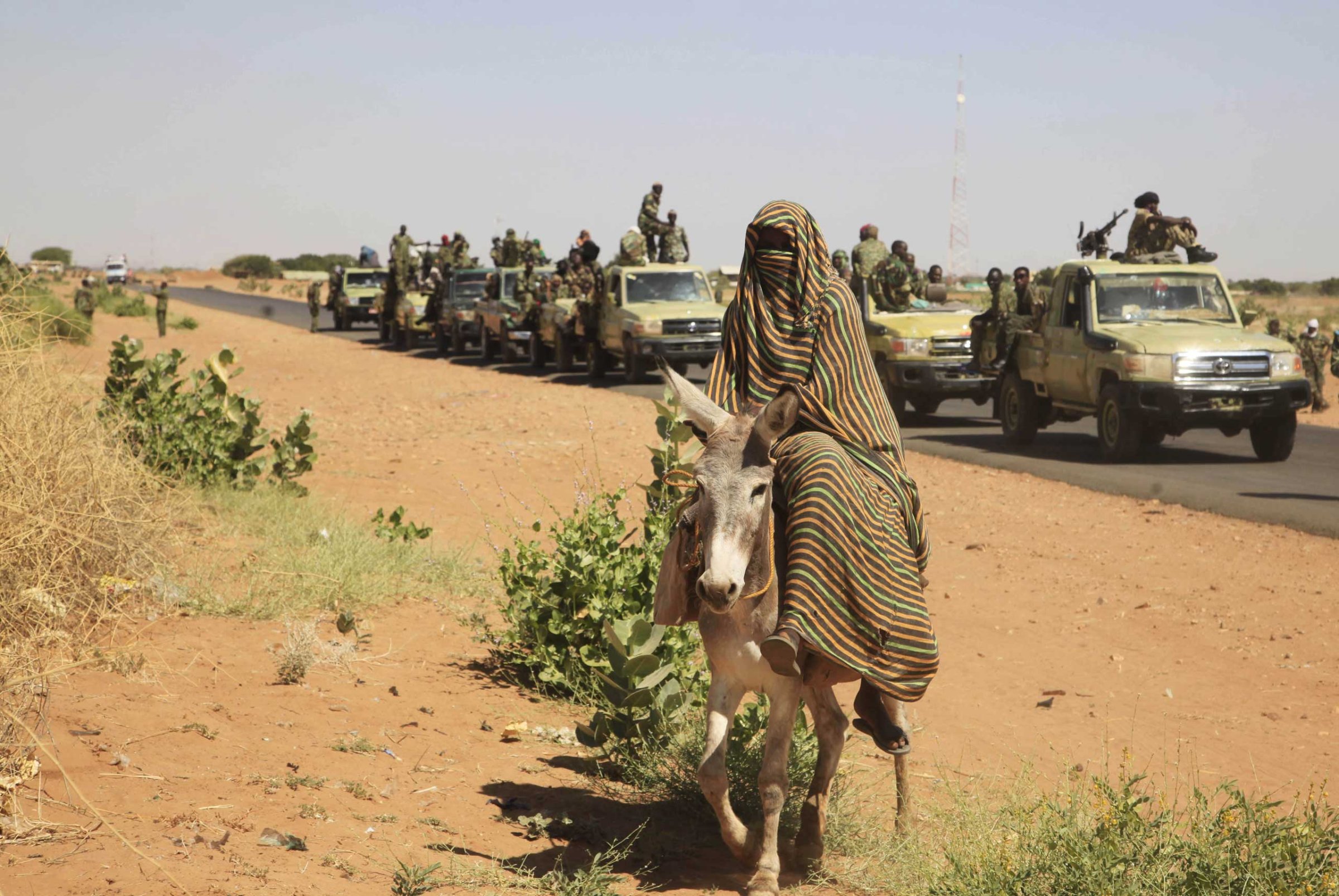 A woman rides a donkey past a convoy of government troops in Tabit village in the North Darfur region of Sudan, Nov, 2014.