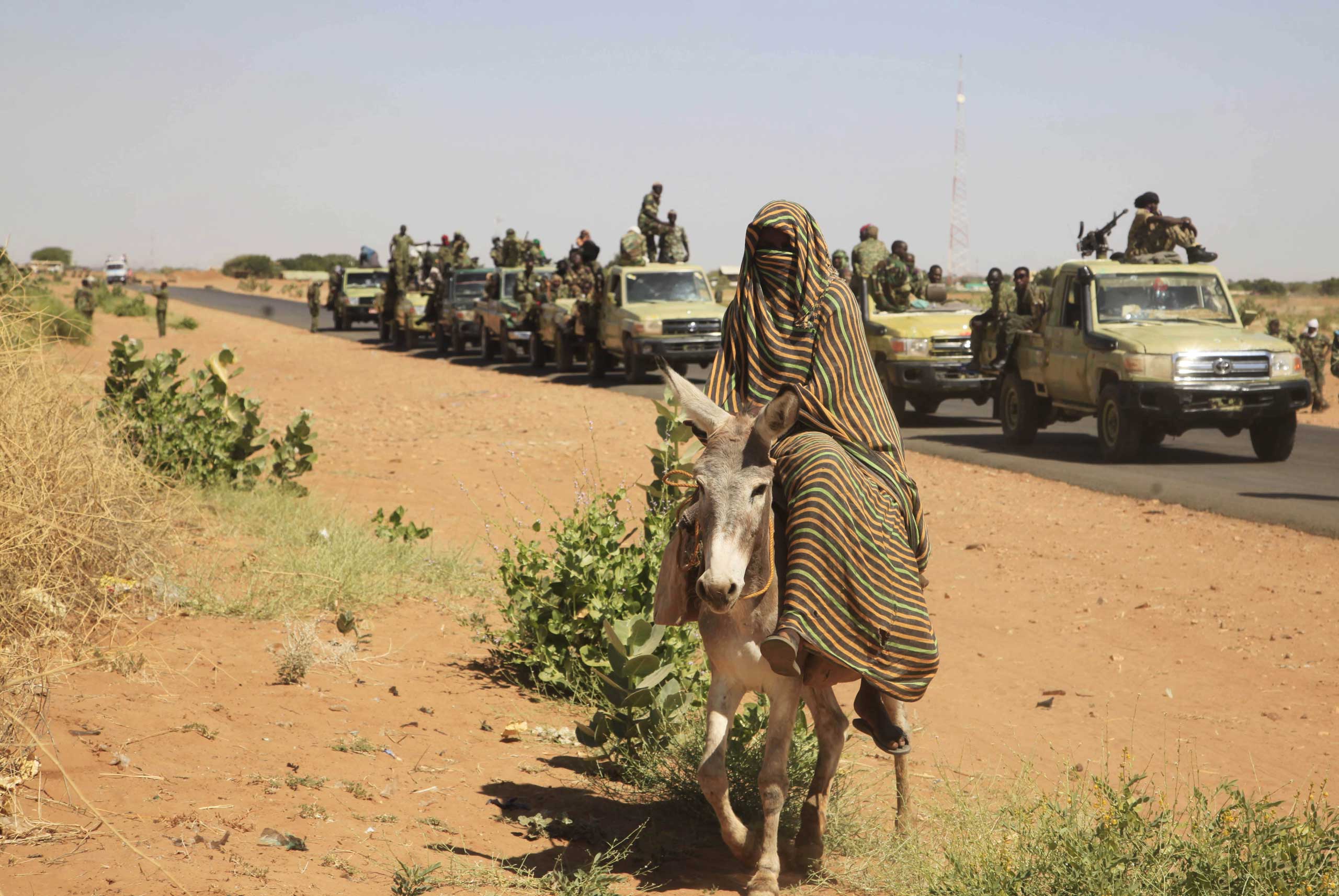 A woman rides a donkey past a convoy of government troops in Tabit village in the North Darfur region of Sudan, Nov, 2014. (Abd Raouf—AP)