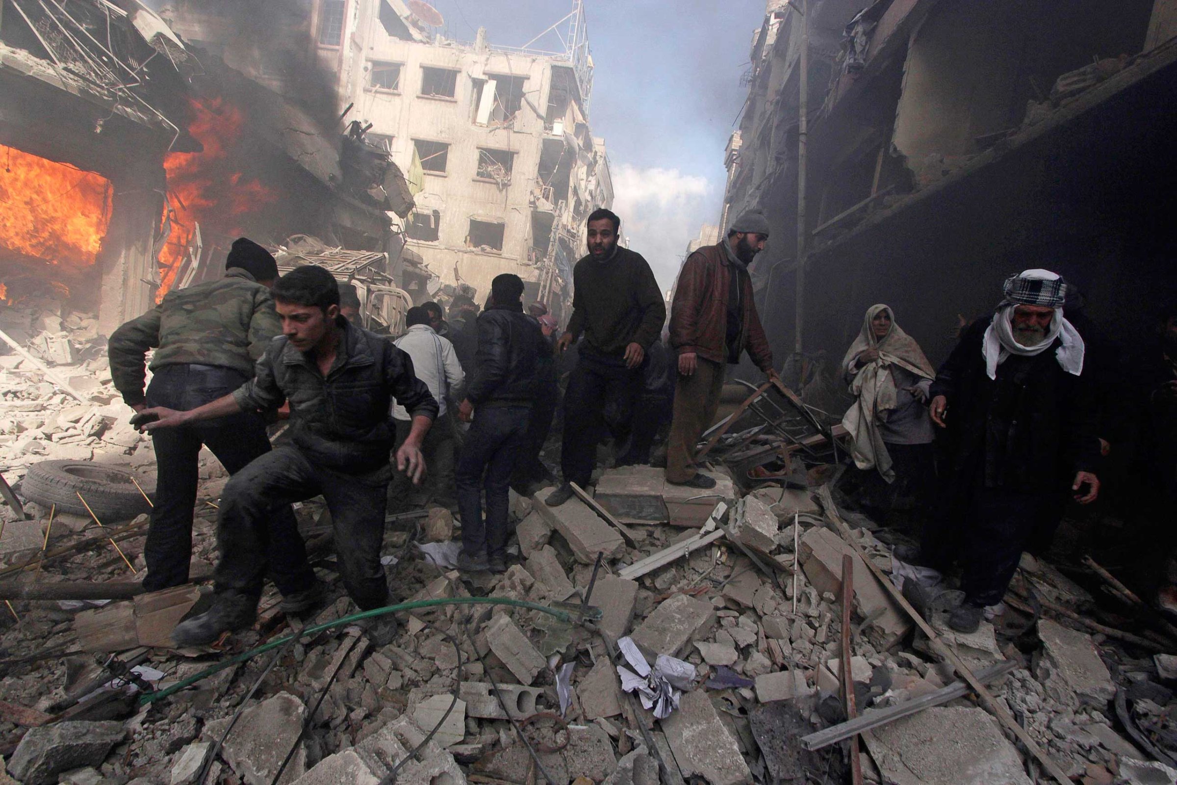 People walk on rubble as others try to put out a fire after what activists said were airstrikes followed by shelling by forces loyal to Syria's President Bashar Assad in the Douma neighborhood of Damascus, Feb. 9, 2015.