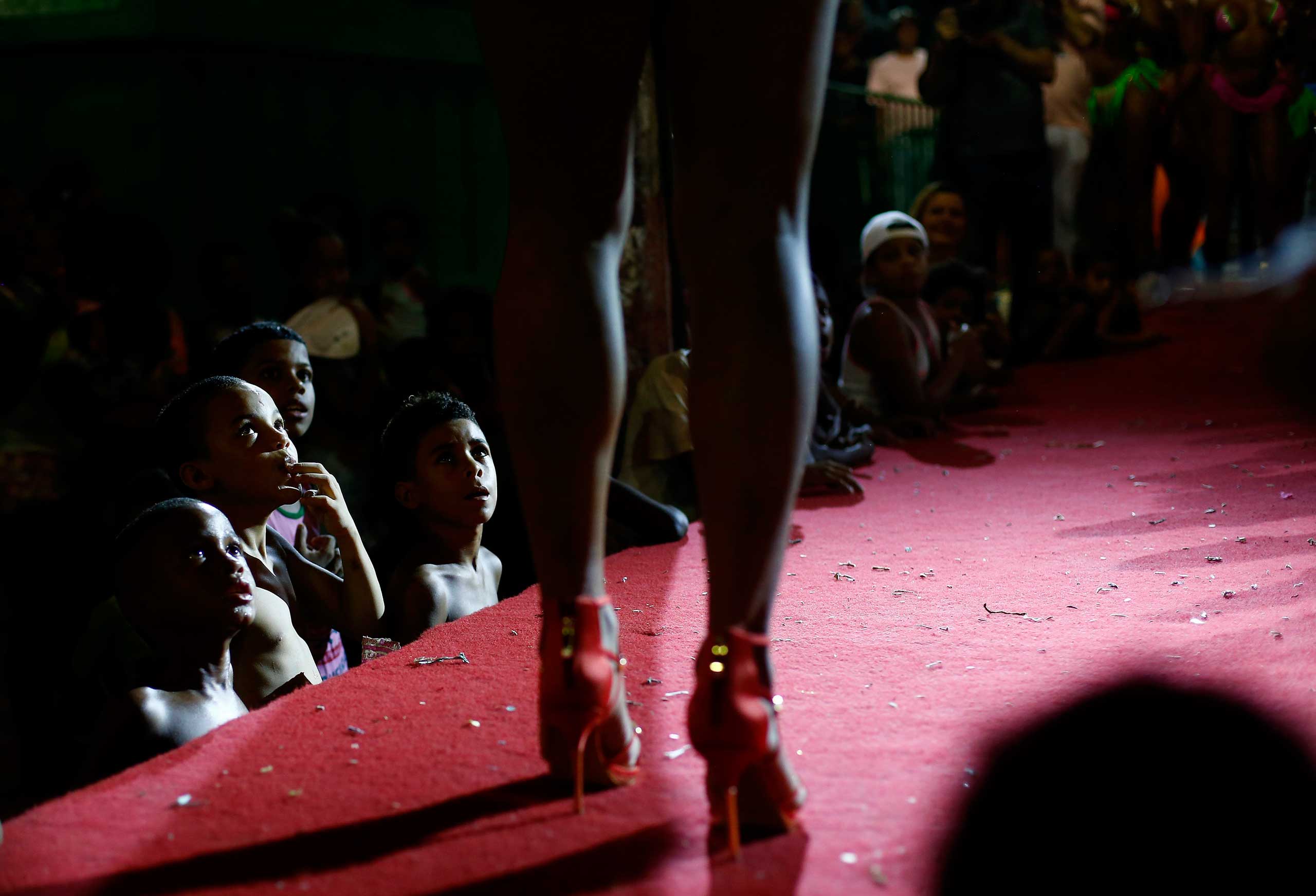 Feb. 11, 2015. Residents of Mangueira slum watch as a participant attends a beauty contest for transvestites and transsexuals at the entrance of the Glam Gay pre-carnival Ball, in Mangueira samba school in Rio de Janeiro.