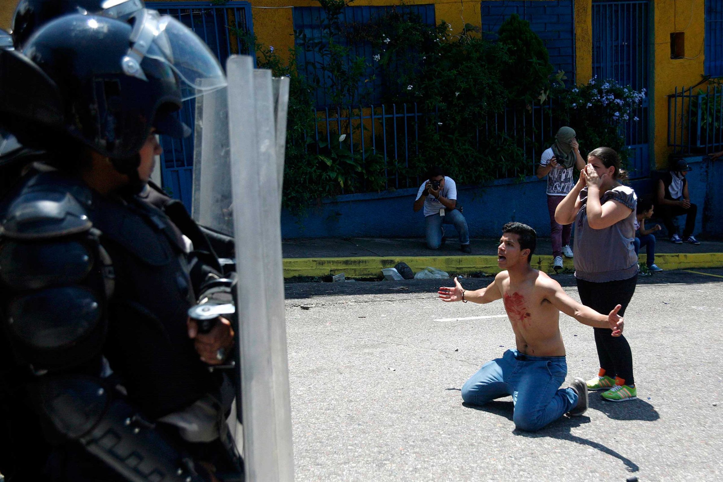 A boy with blood on his chest kneels in front of police after 14-year-old student Kluiver Roa died during a protest in San Cristobal, Venezuela, Feb. 24, 2015.