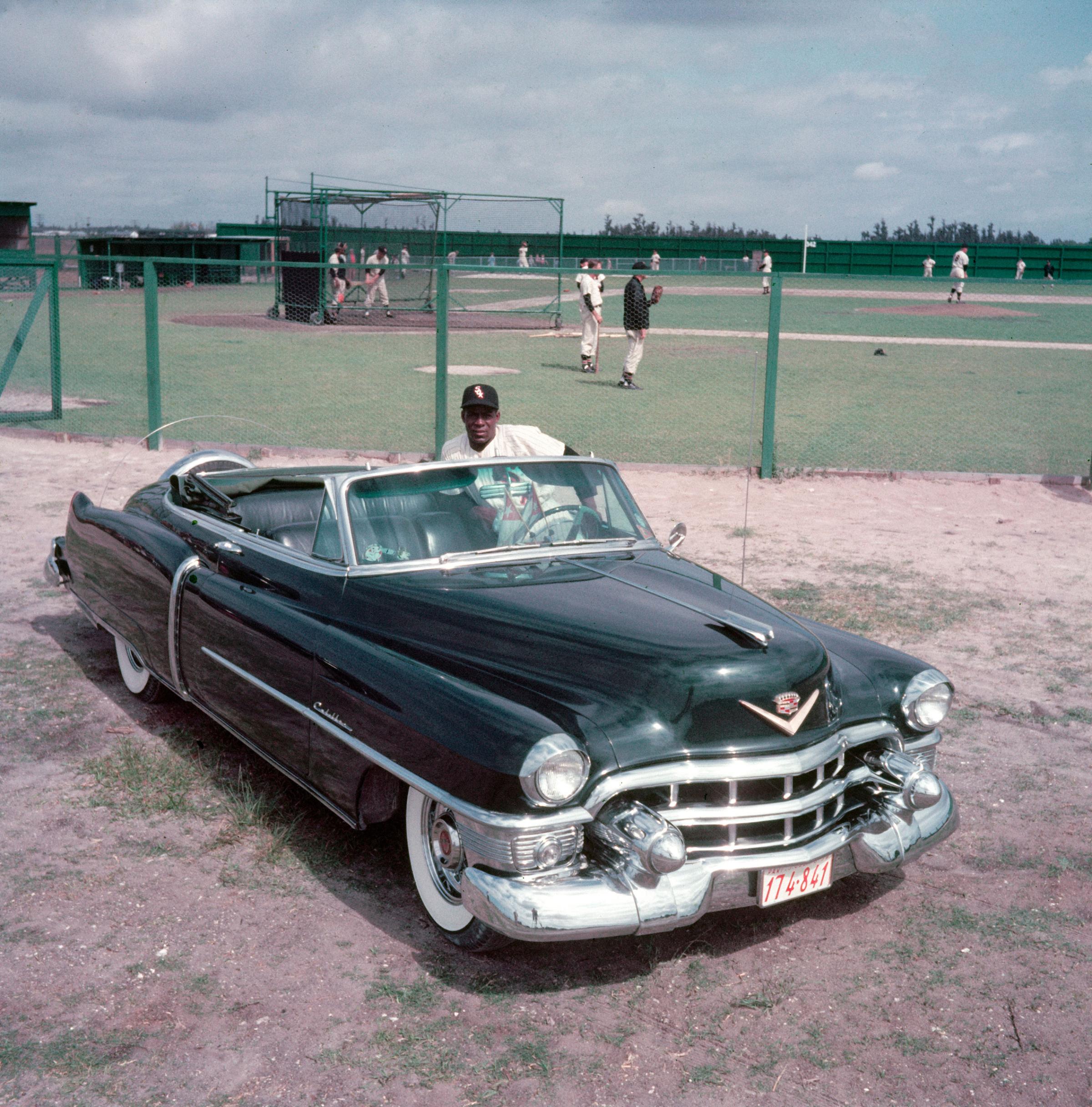 Minnie Minoso posing next to brand new Cadillac convertible during spring training, 1954.